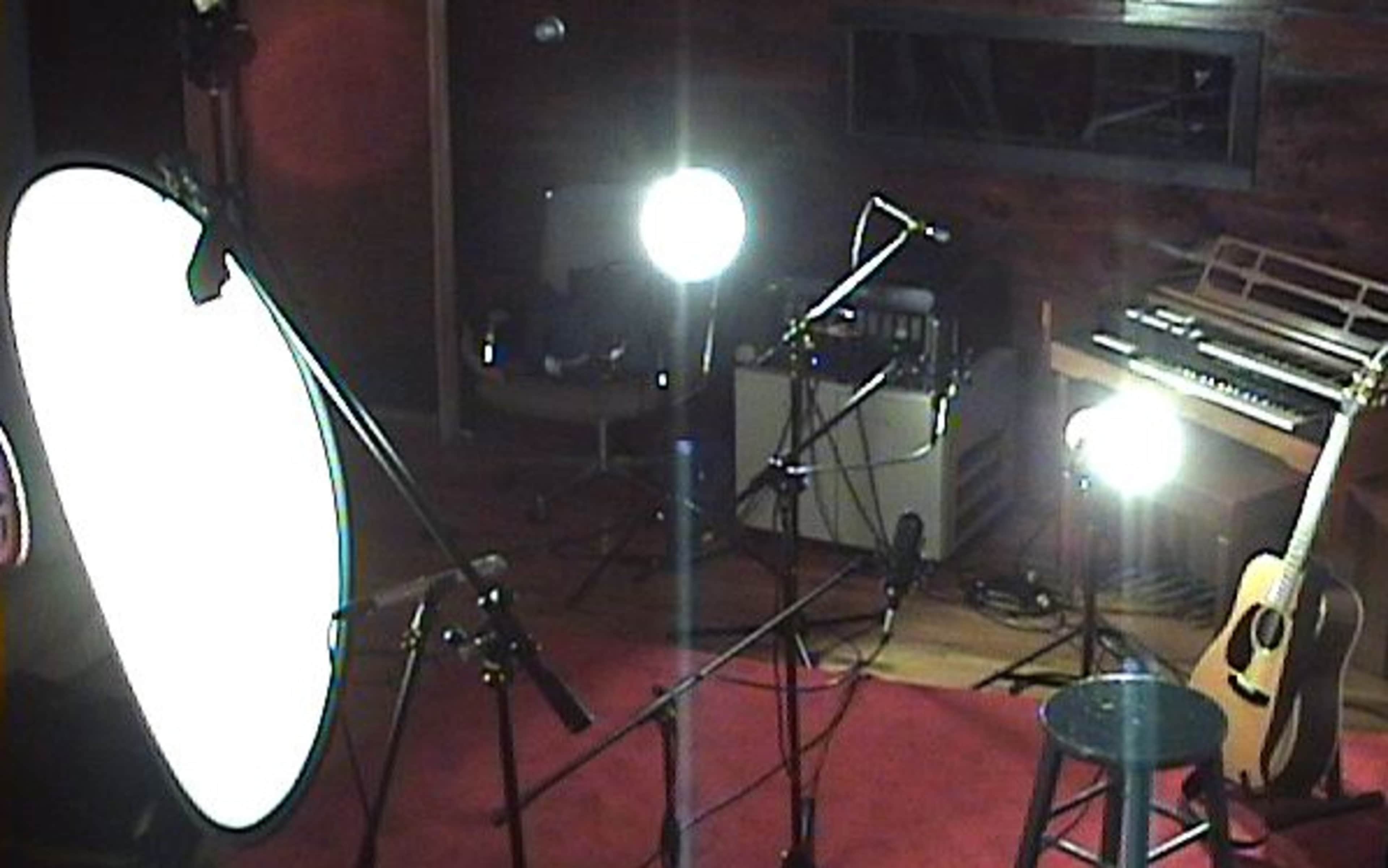 A recording studio setup with studio lights, microphones, and an acoustic guitar placed next to a stool.