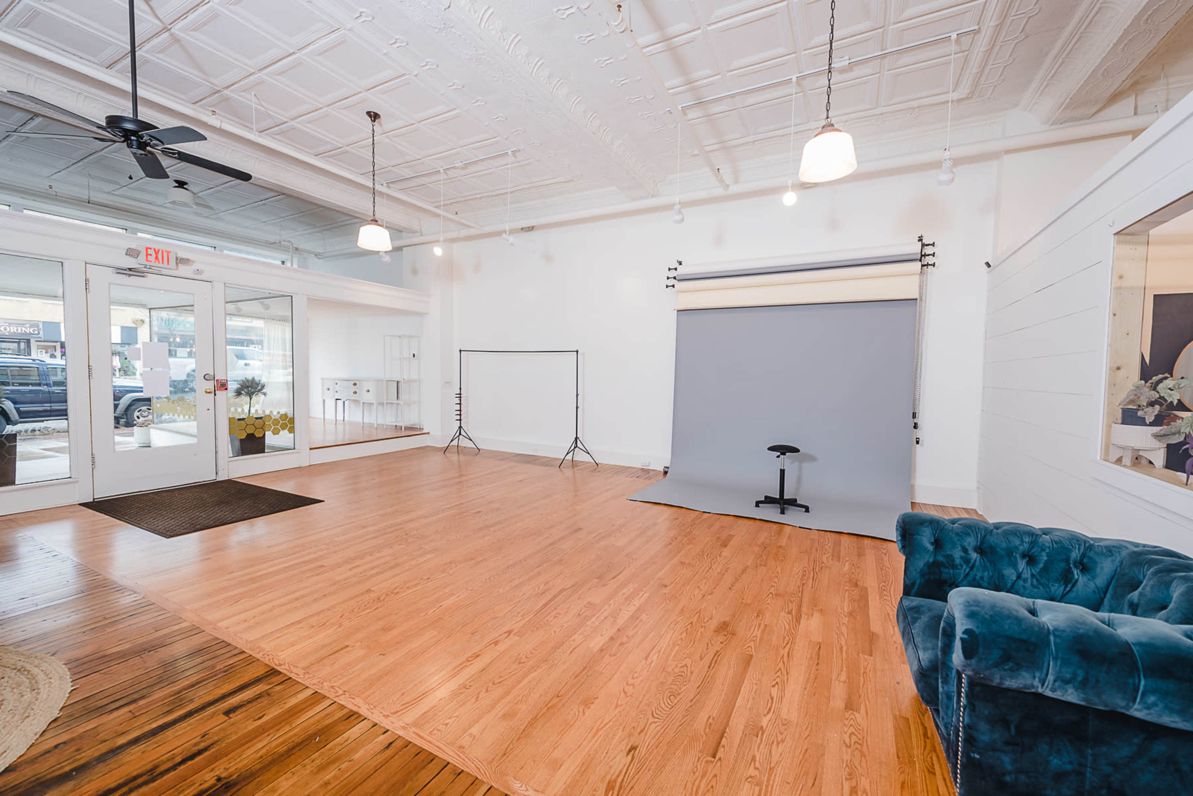 A spacious indoor photography studio featuring a gray backdrop, wooden floors, and a blue couch.
