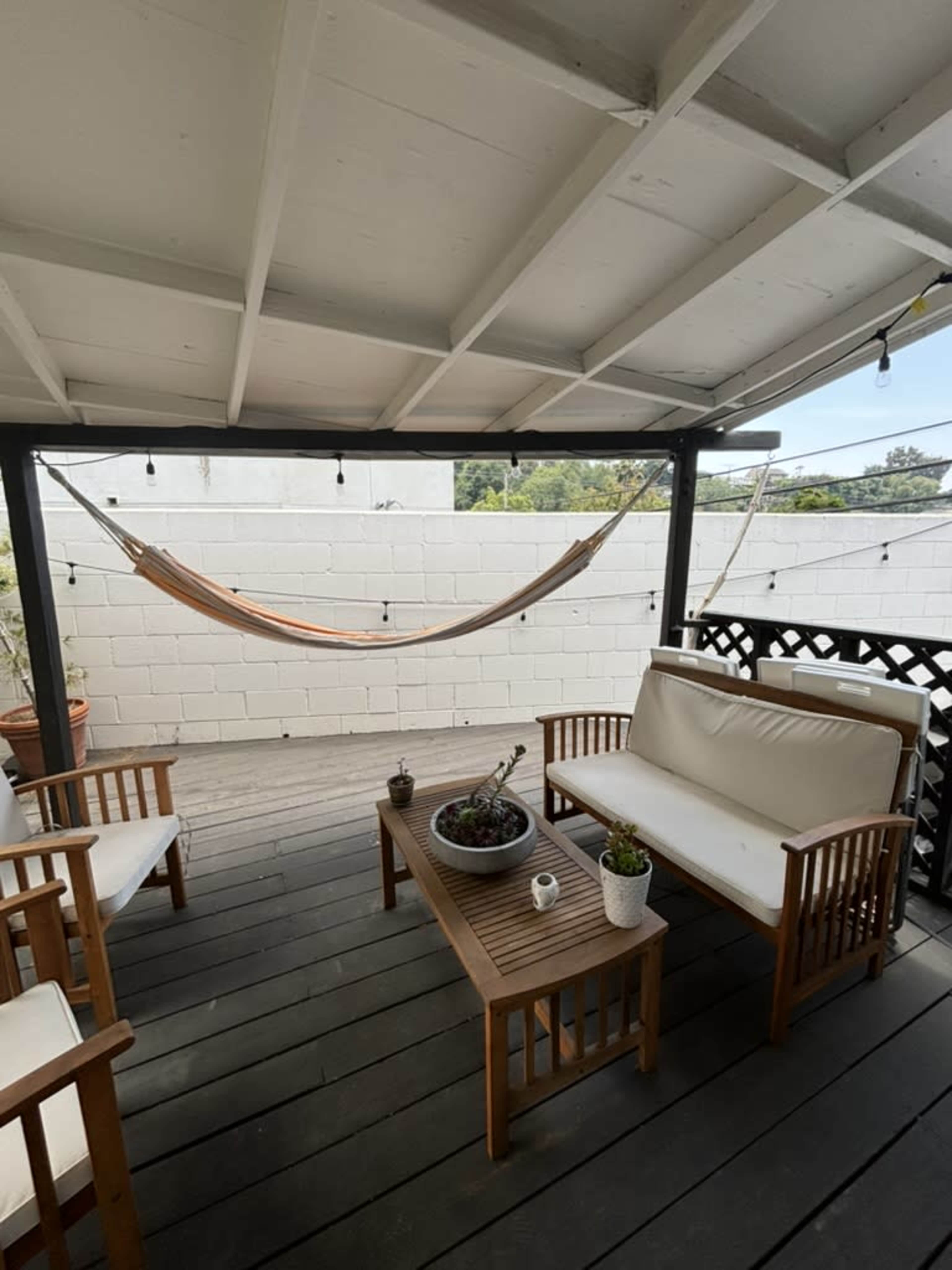 A covered patio features a hammock, a wooden coffee table with plants, and several seating areas.