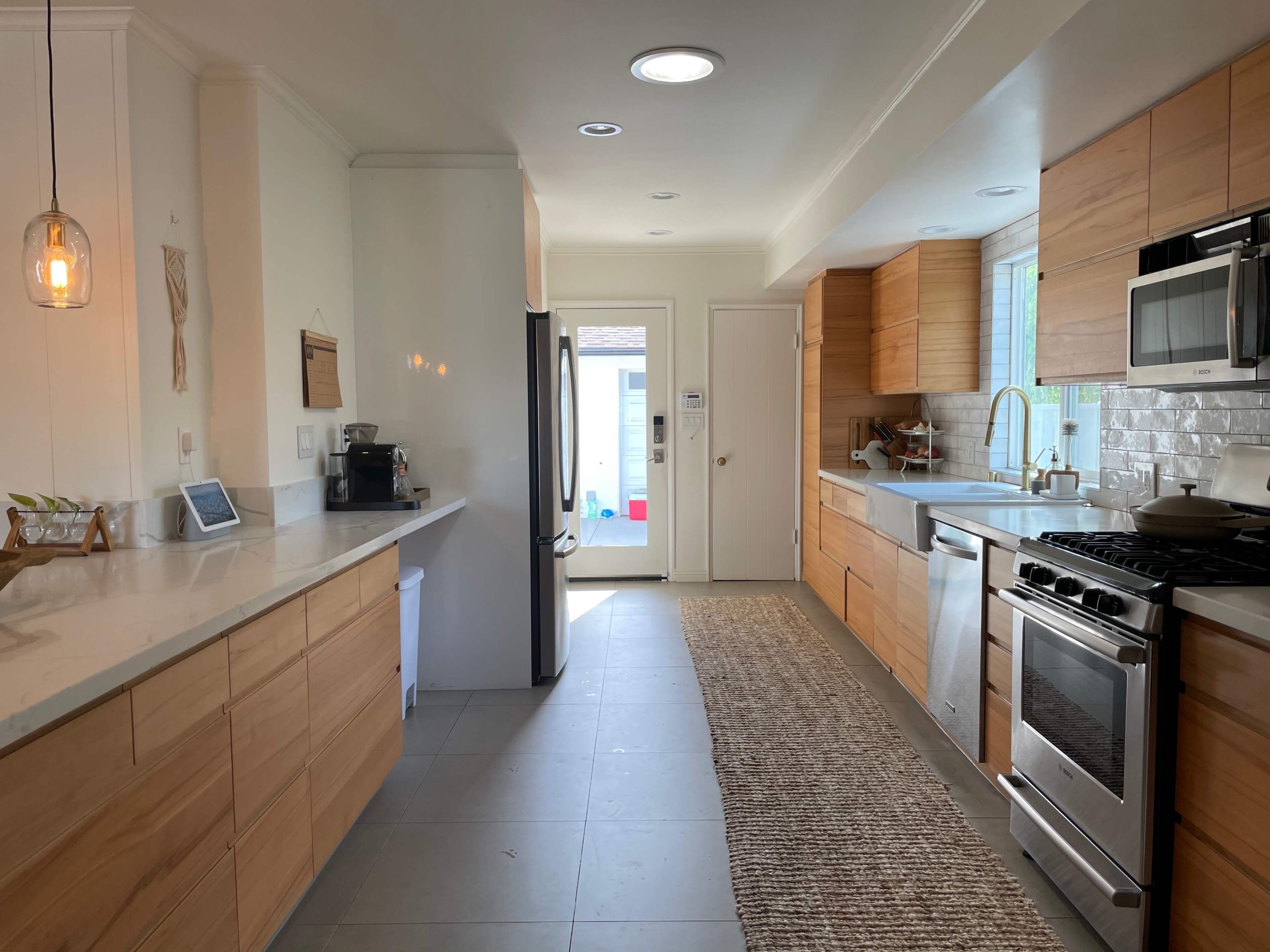 The image shows a modern kitchen with wooden cabinets, a stainless steel stove, and a door leading to the outside.