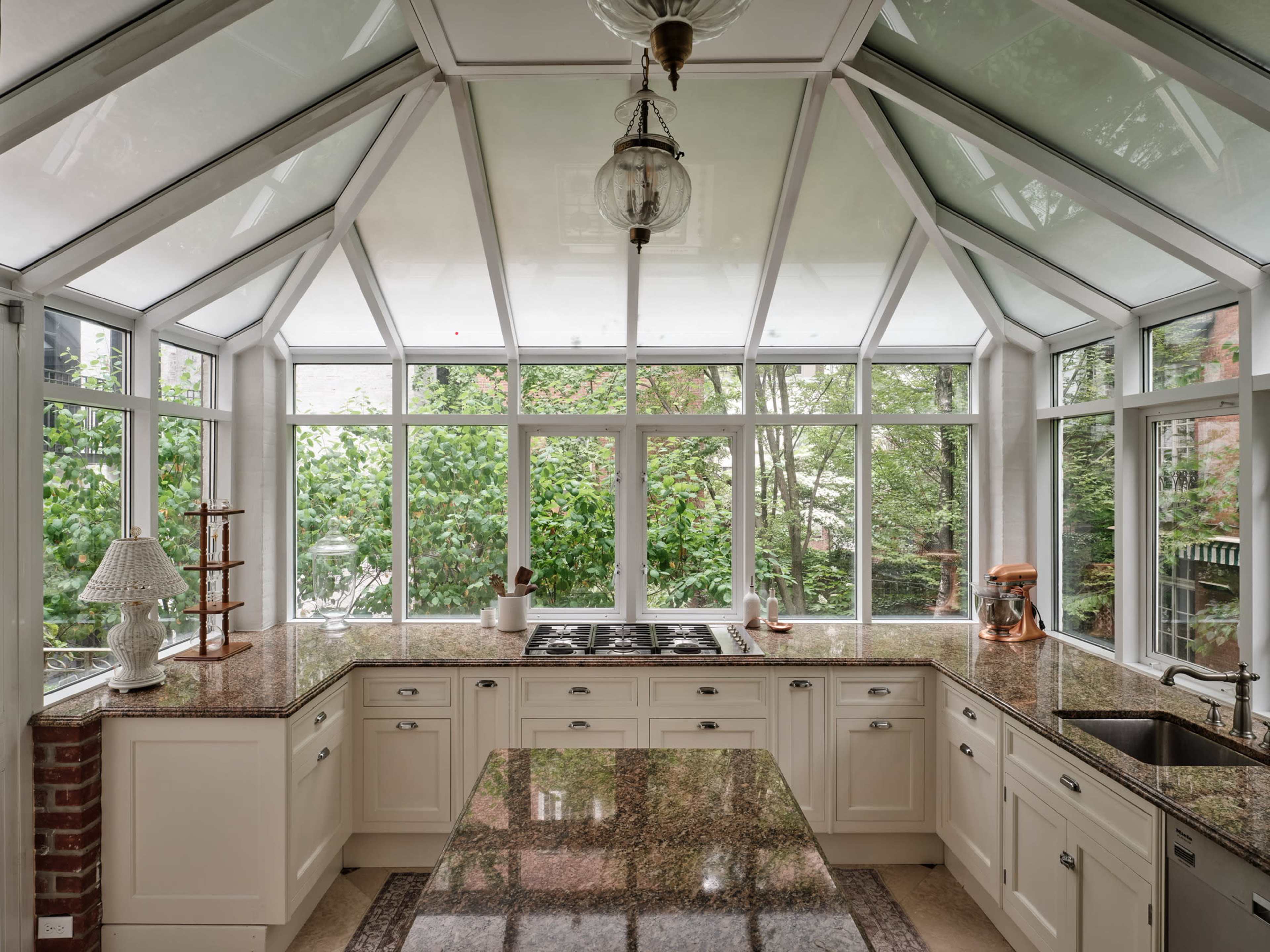 A bright kitchen features large windows that provide a view of greenery outside, with a central island and modern appliances.