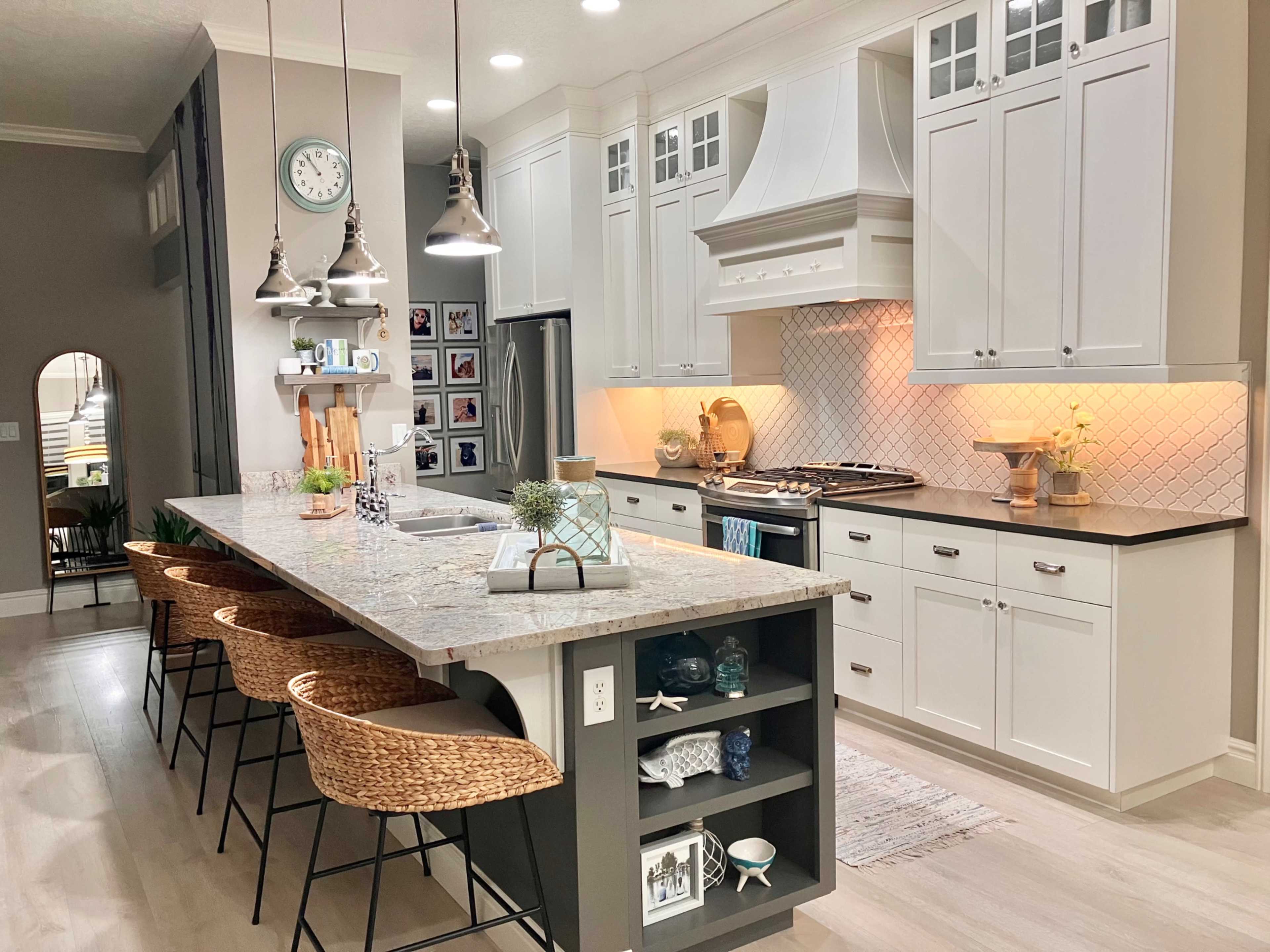 A modern kitchen features white cabinetry, a large island with bar stools, and stainless steel appliances, highlighted by warm lighting and decorative accents.