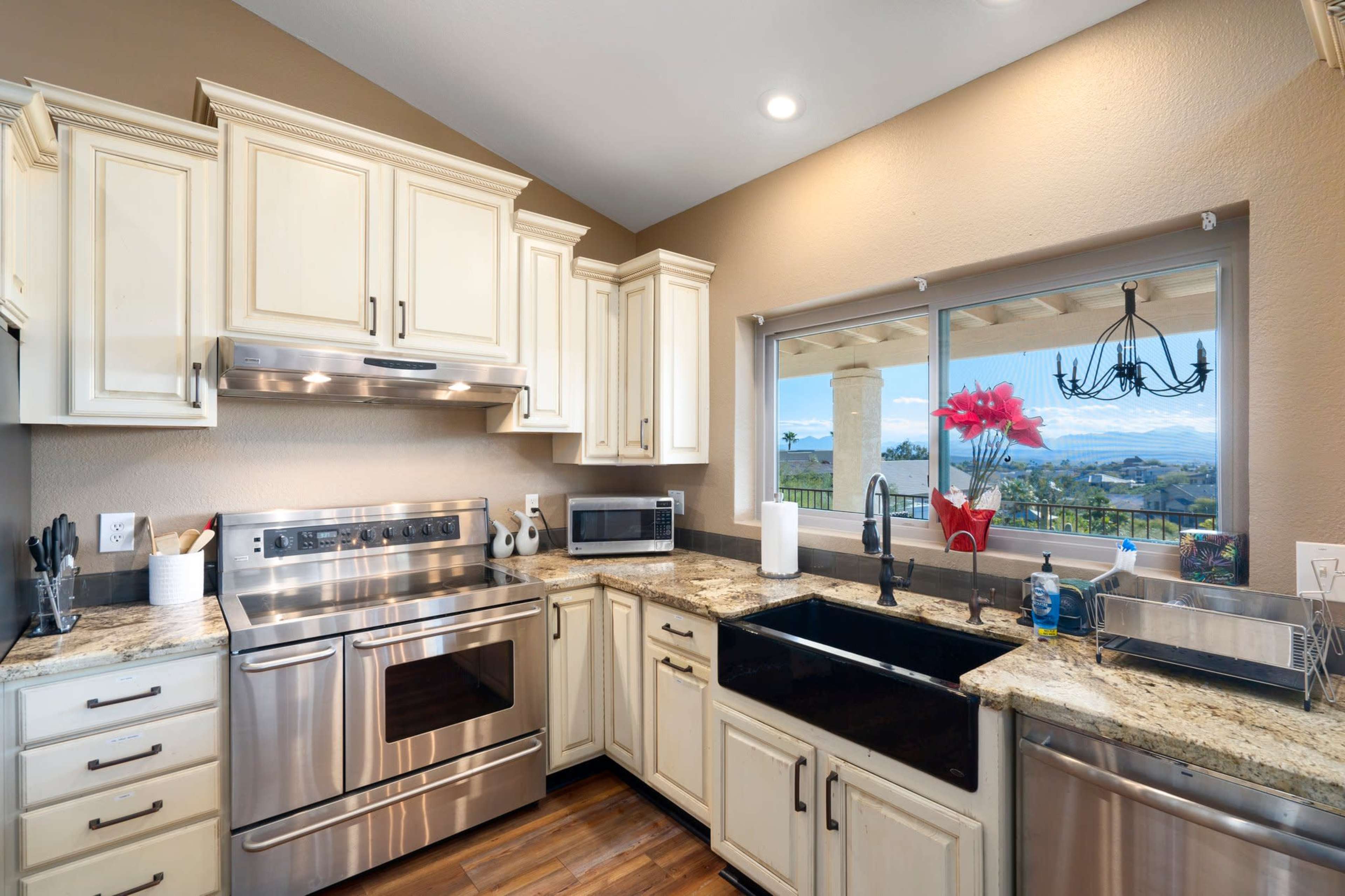 A modern kitchen features cream-colored cabinetry, stainless steel appliances, granite countertops, and a large window with a view.