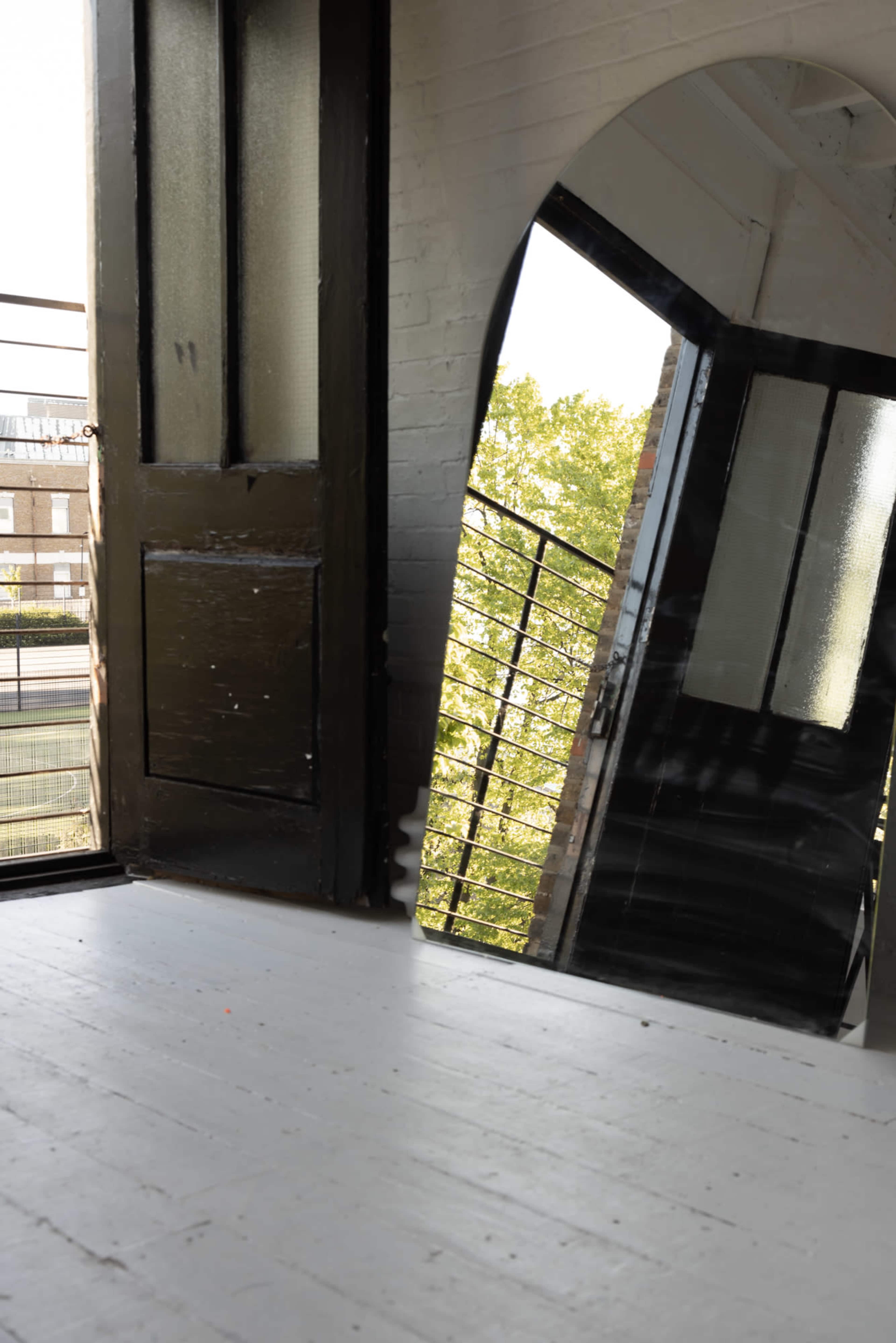 A large, angled mirror leans against a wall next to an open door, revealing a bright outdoor view through the doorway.