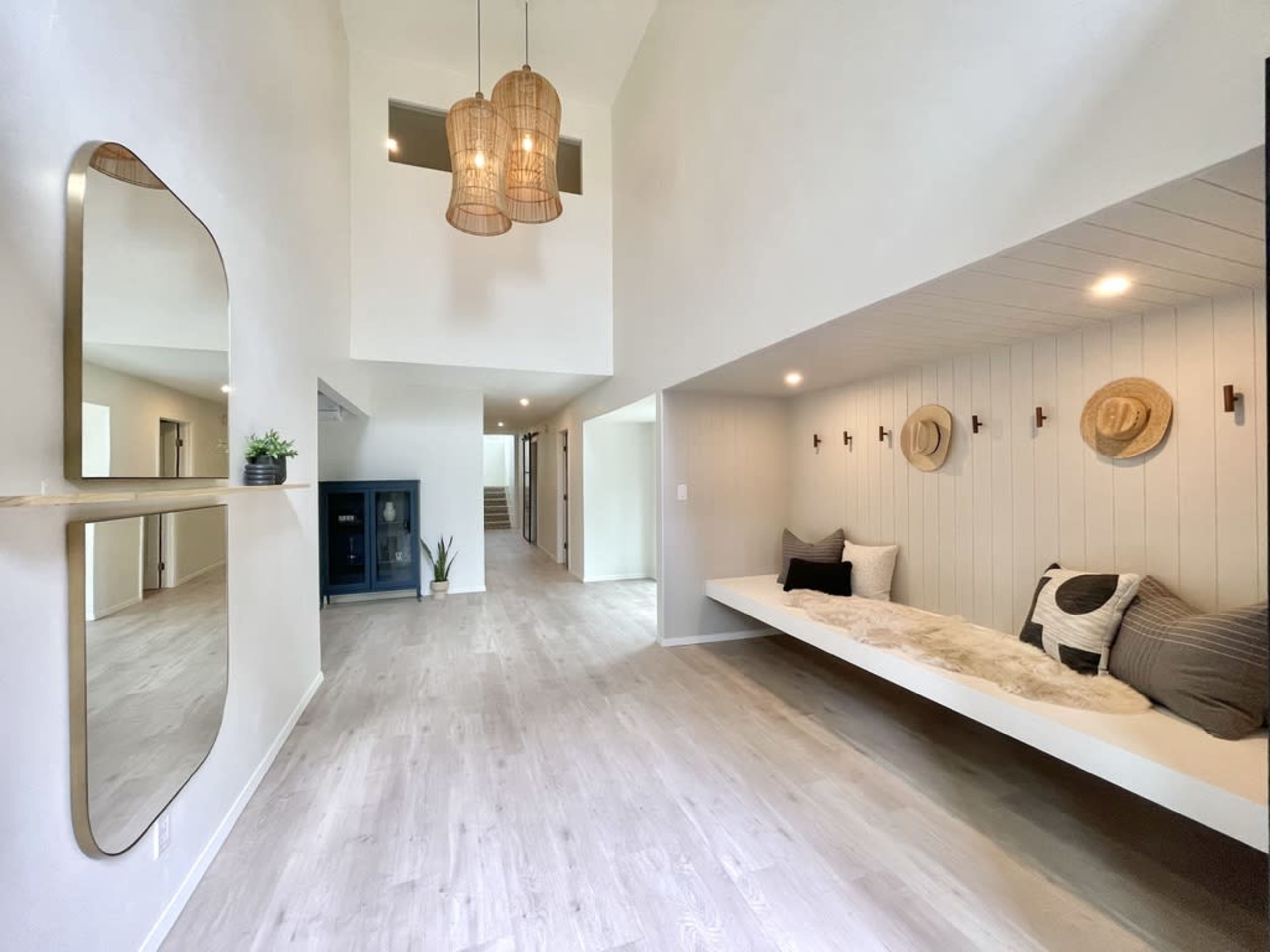 A spacious, modern interior with a seating nook, pendant lights, and a large mirror on one wall.