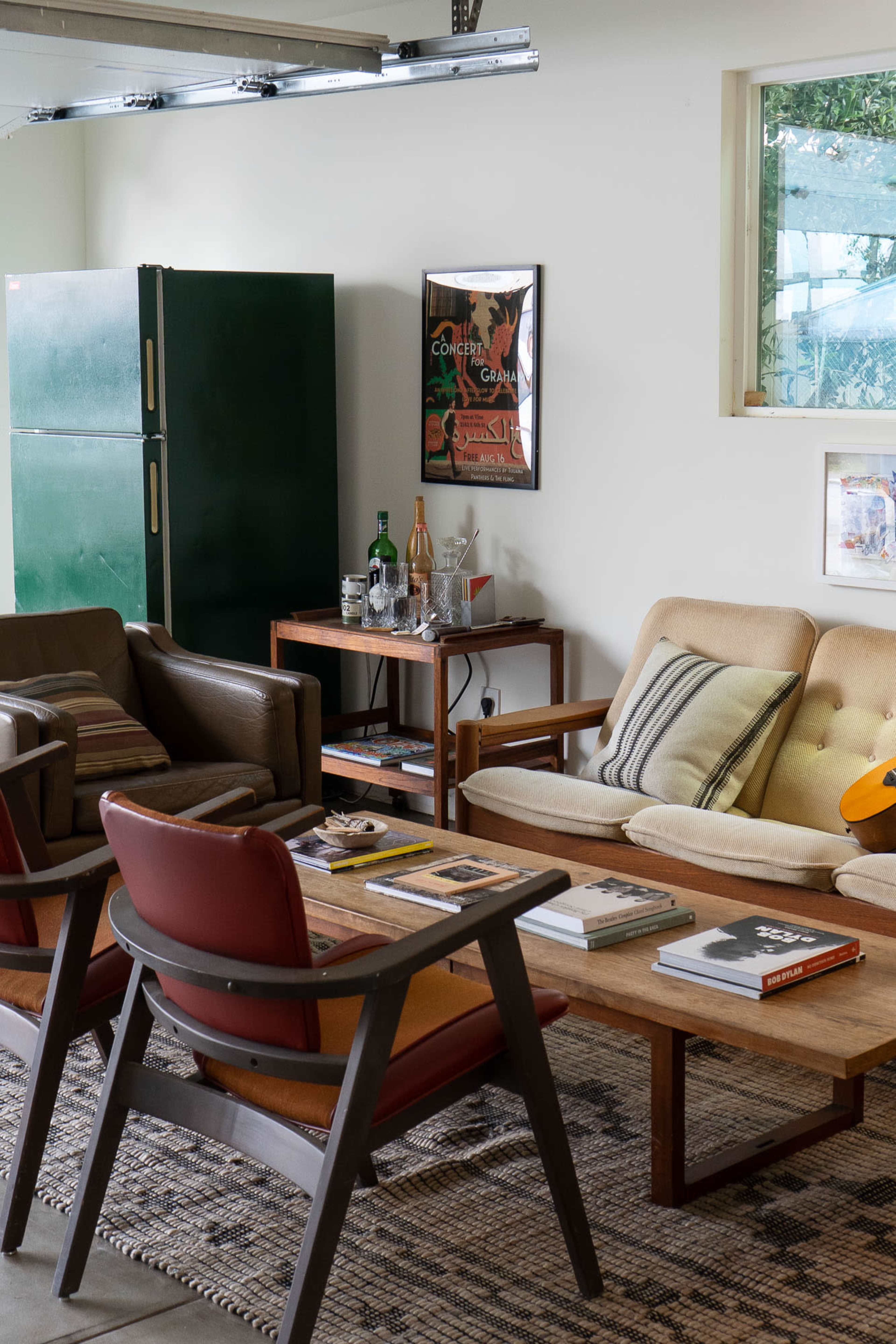 The image shows a living space furnished with a beige couch, two brown armchairs, a coffee table with magazines, and a green refrigerator in the background.