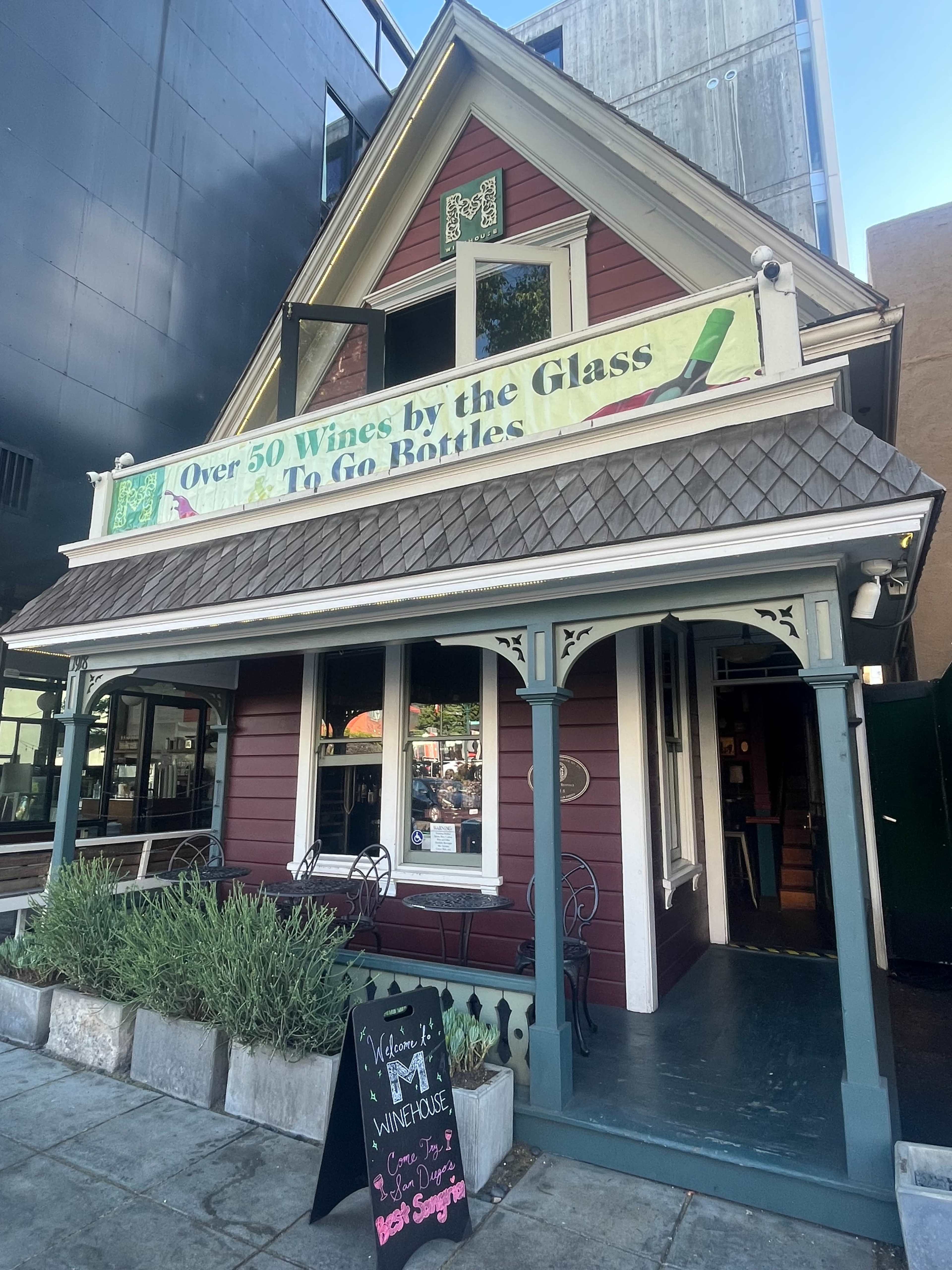 The image shows a two-story red and white building with a sign promoting over 50 wines by the glass and to-go bottles.