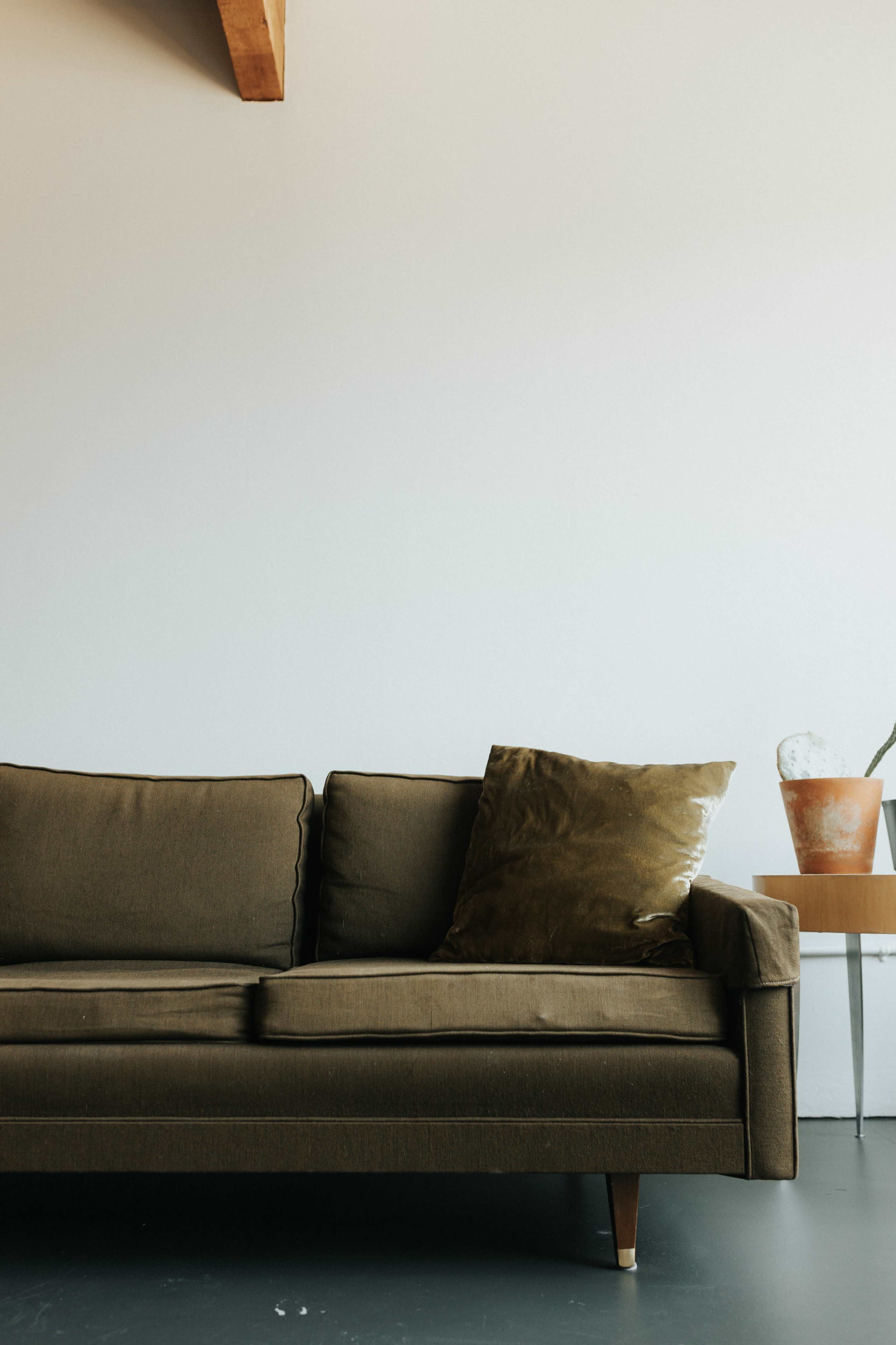 A green sofa with a decorative pillow sits beside a small wooden table.