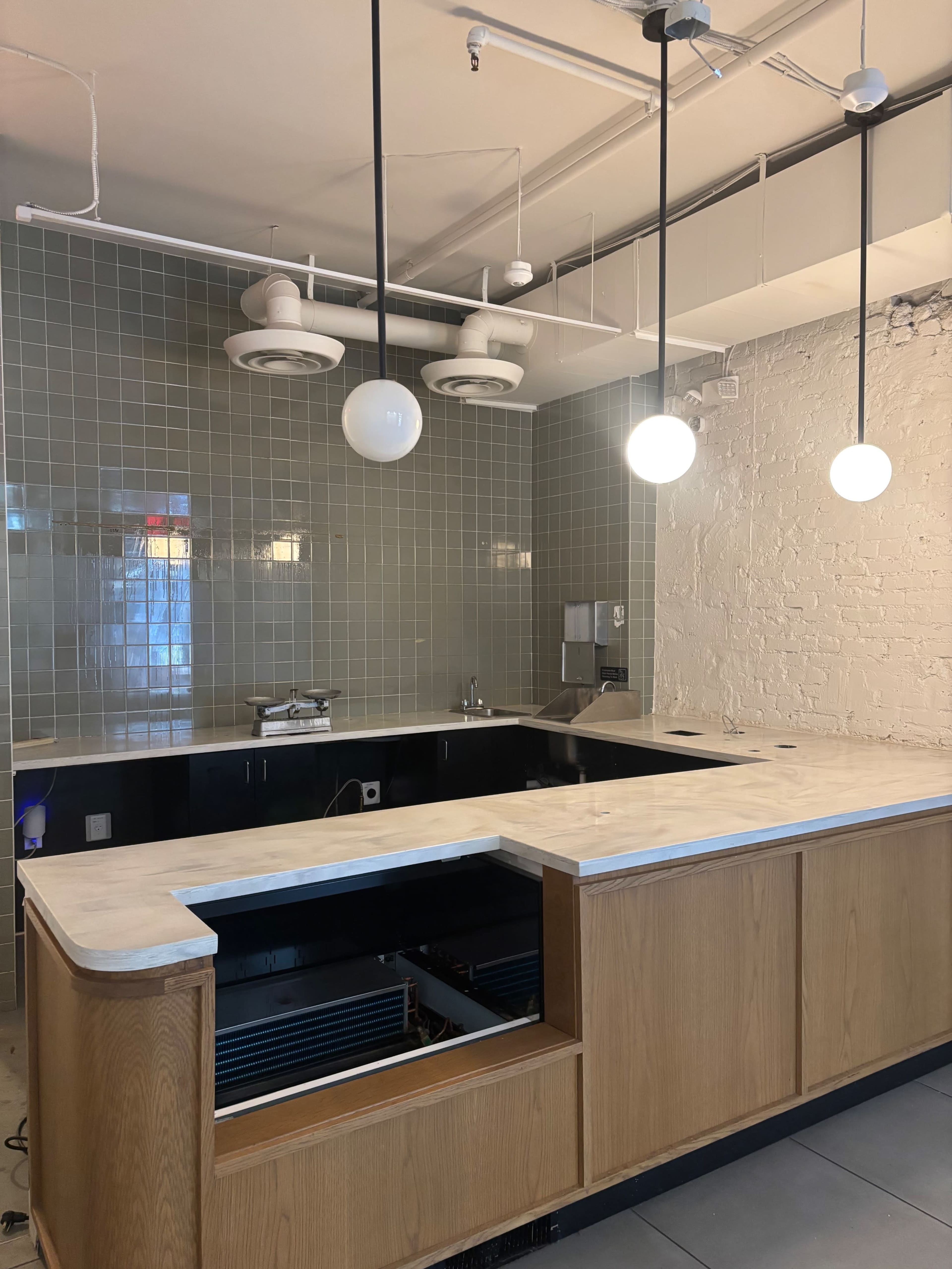 The image shows a modern kitchen with a marble countertop, wall tiles in muted colors, and pendant lights hanging from the ceiling.