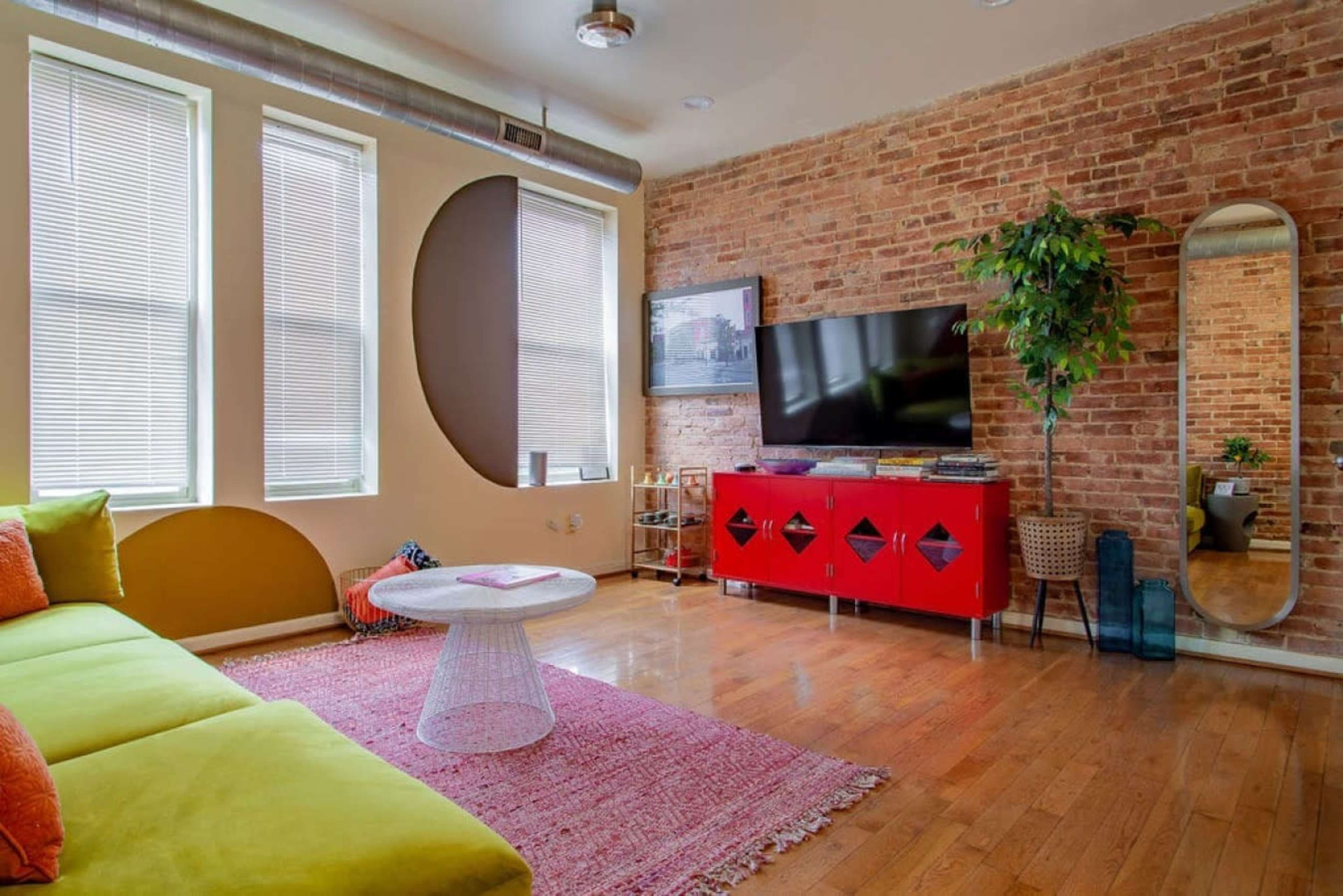 A stylish living room featuring a brick wall, a green sofa, a circular coffee table, and a red TV stand with decorative elements.