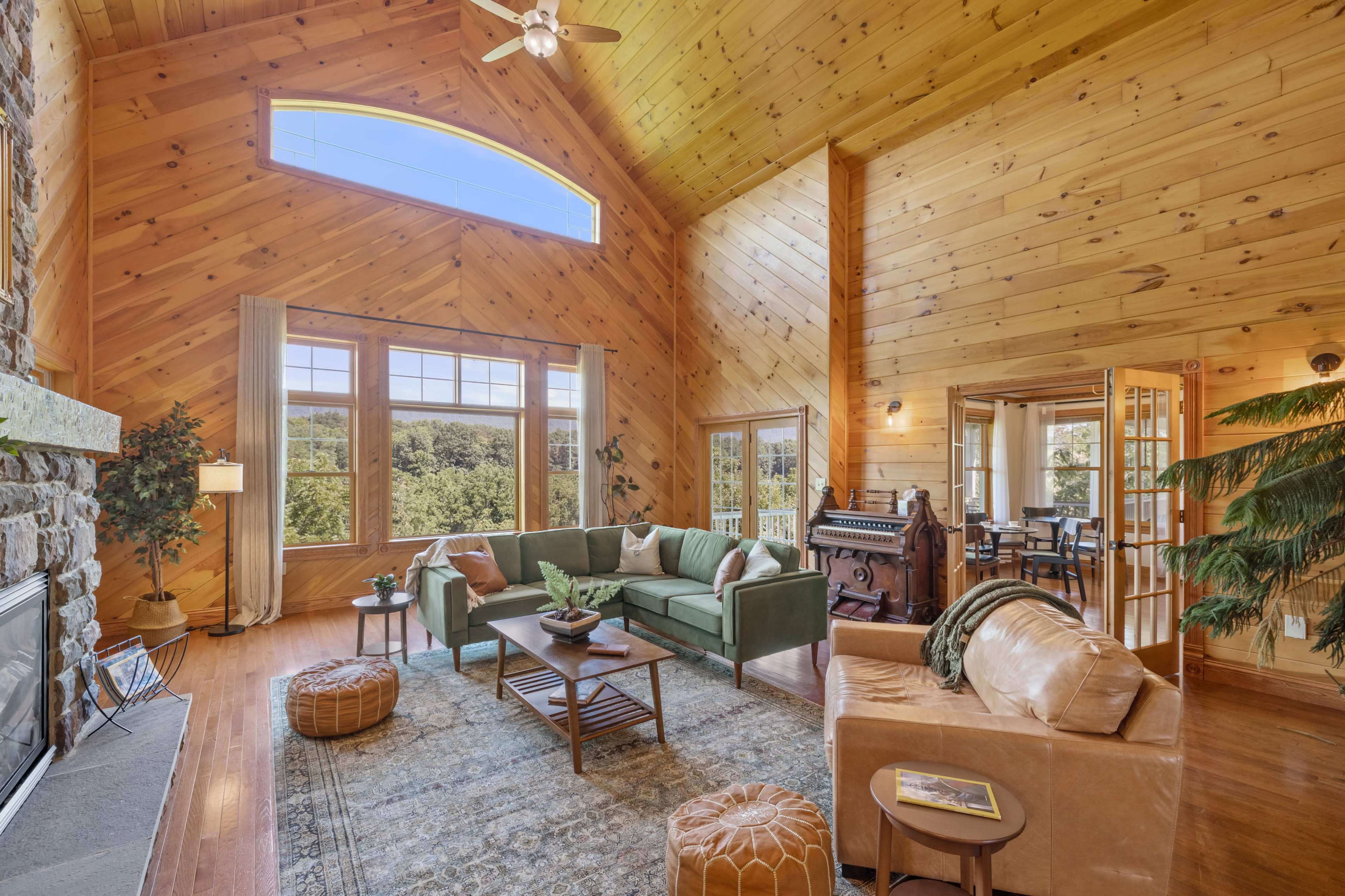 The room features a high ceiling with wooden beams, large windows showcasing a view of the outdoors, and a mix of comfortable seating arrangements.