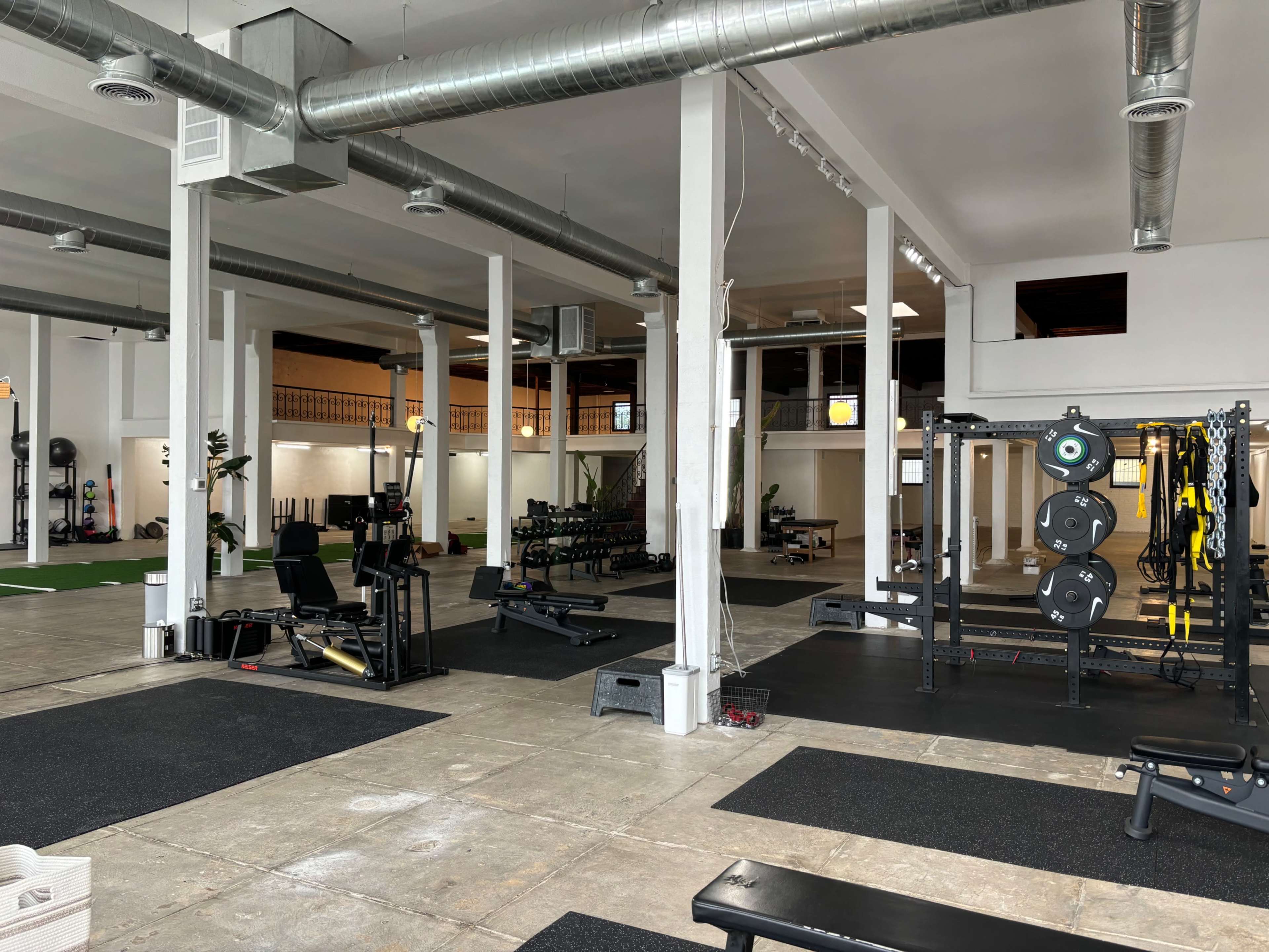 A spacious gym with various workout equipment, including weight benches and a squat rack, set in an open-layout environment.