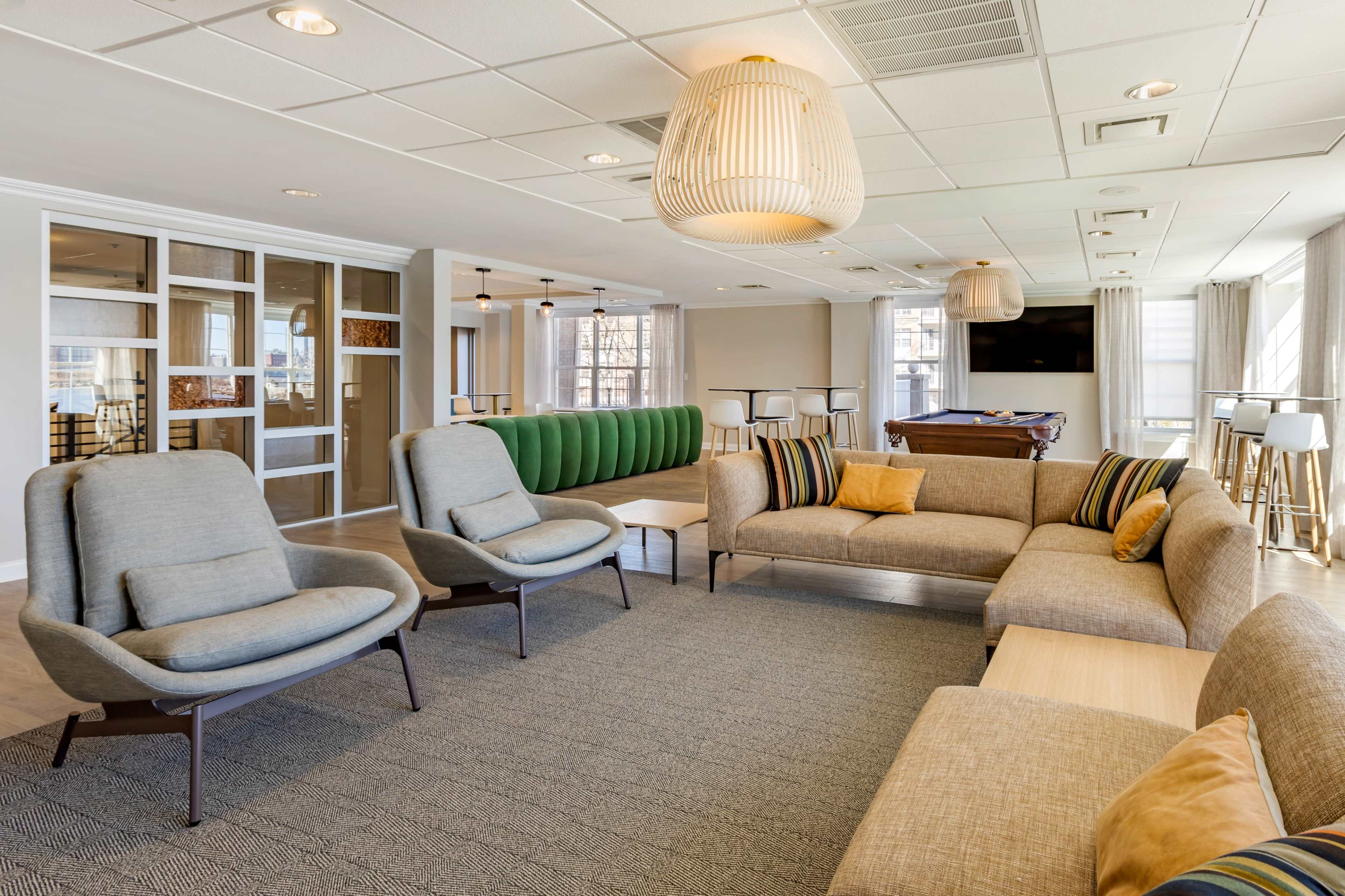 A modern lounge area with a combination of comfortable seating, wooden tables, and large windows letting in natural light.