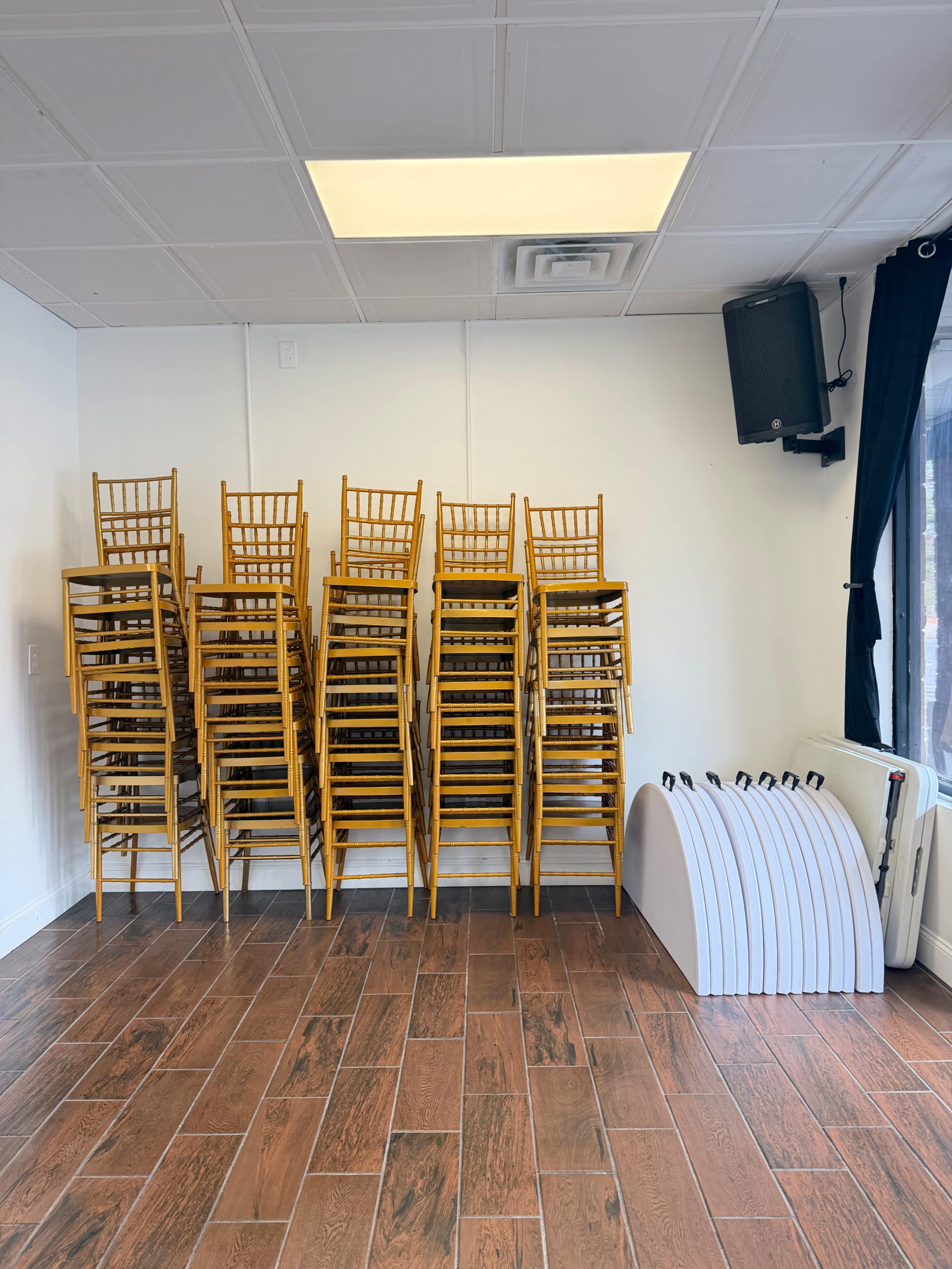 A stack of yellow chairs is arranged against a white wall, with a set of white folding tables resting nearby.