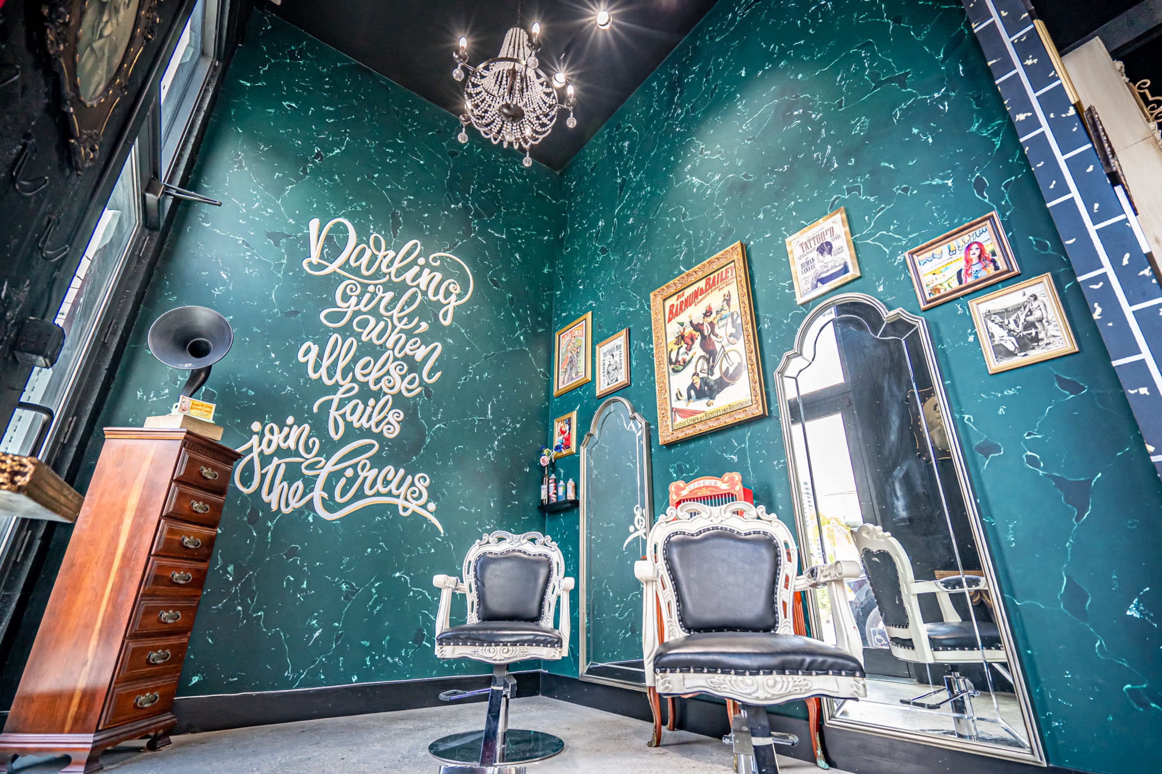 A vintage-style hair salon features ornate mirrors, elegant chairs, and a large green wall with decorative text.