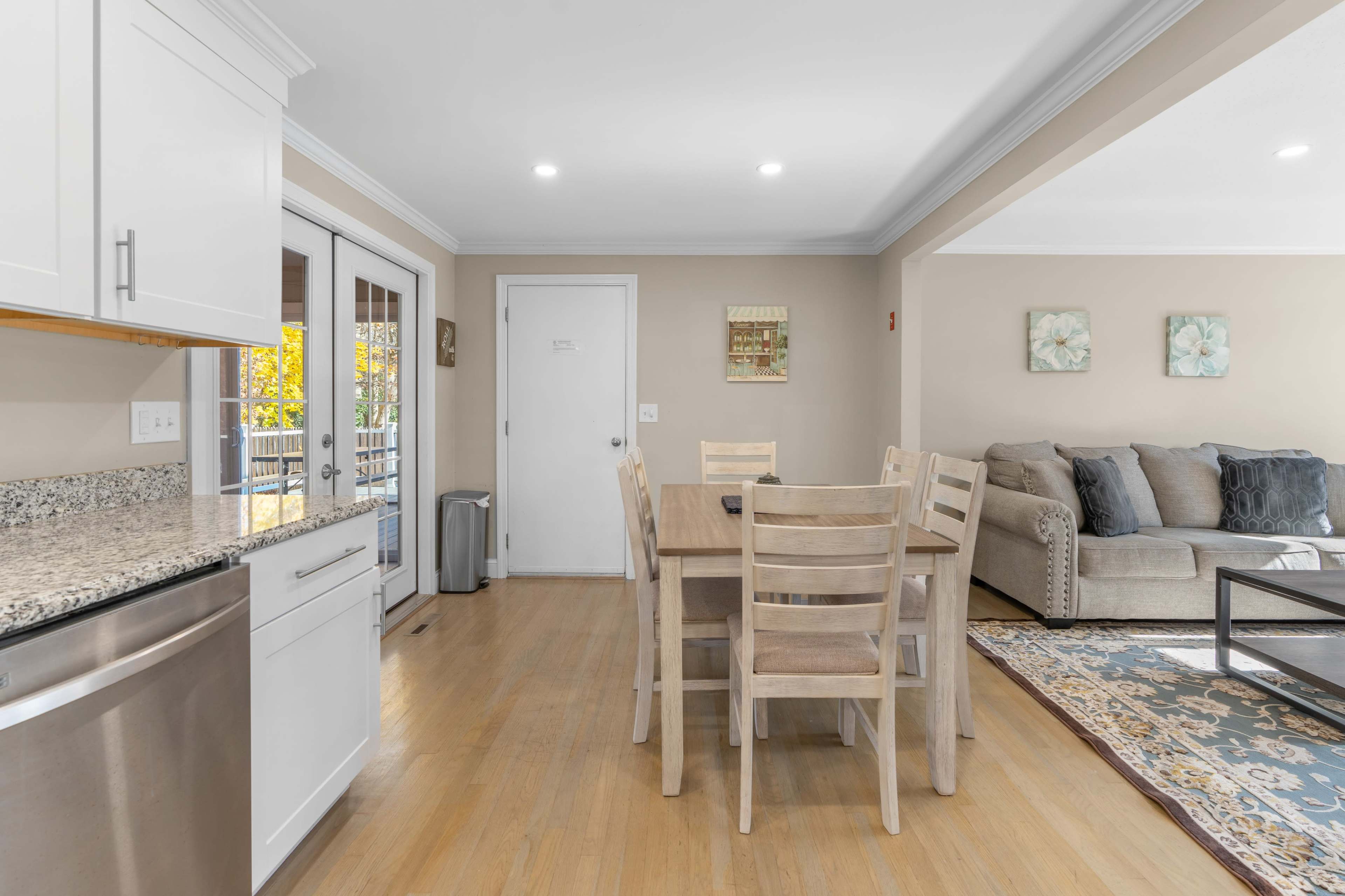 A modern kitchen and dining area with a wooden table and a living room featuring a gray sofa and decorative elements.