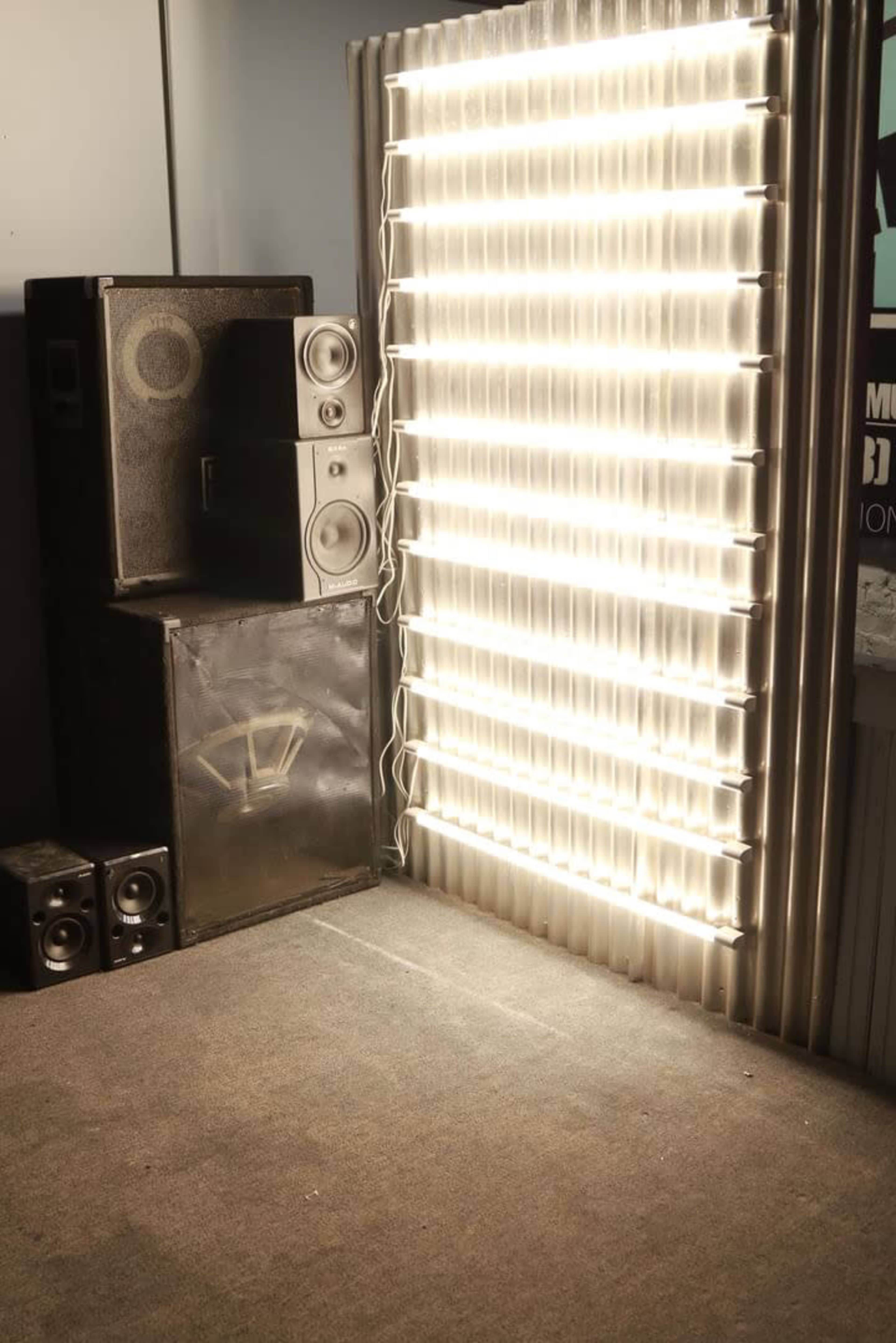 A corner of a room with stacked audio speakers next to a wall illuminated by bright neon lights.