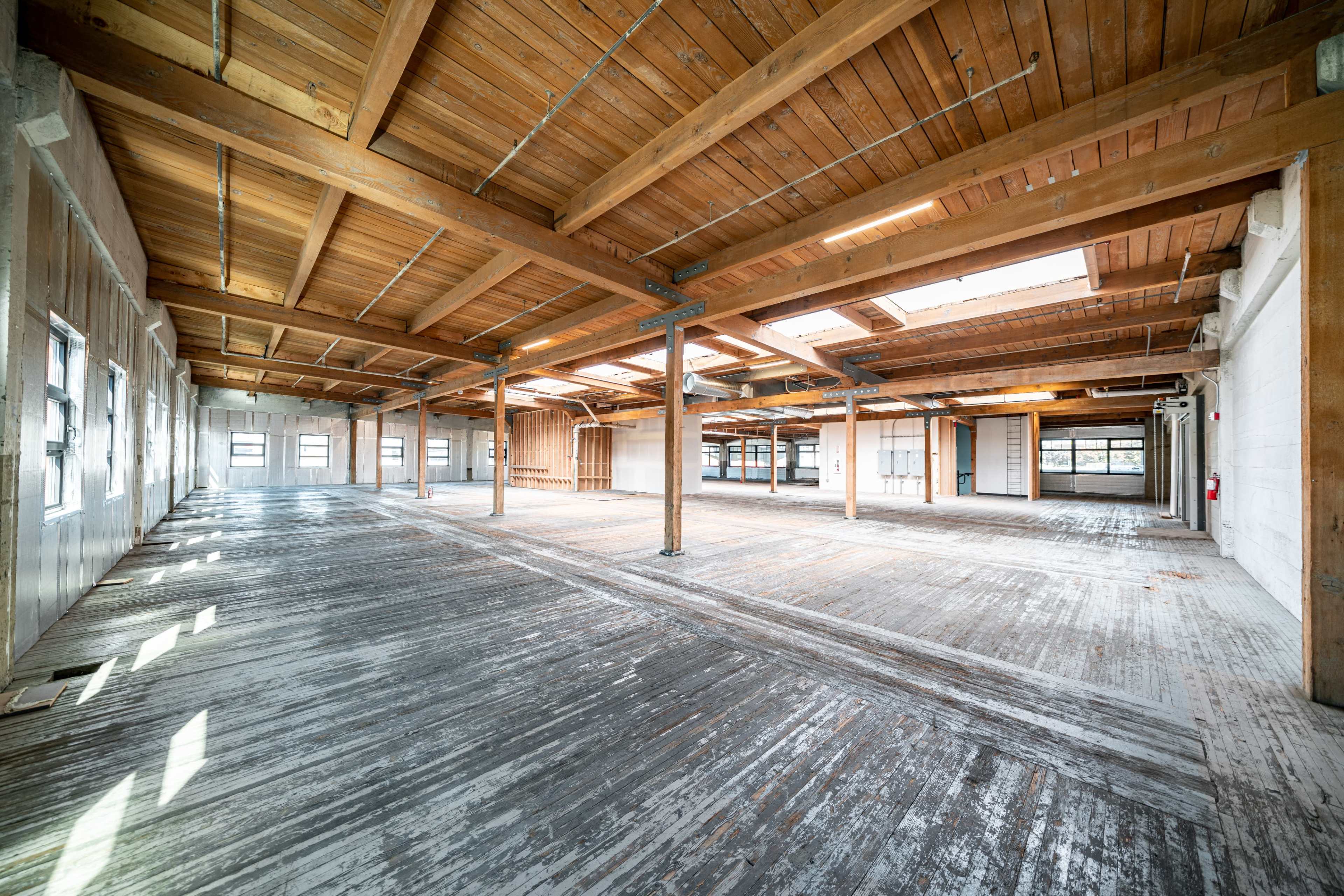 A spacious, empty interior of a building with exposed wooden beams and a wooden floor.