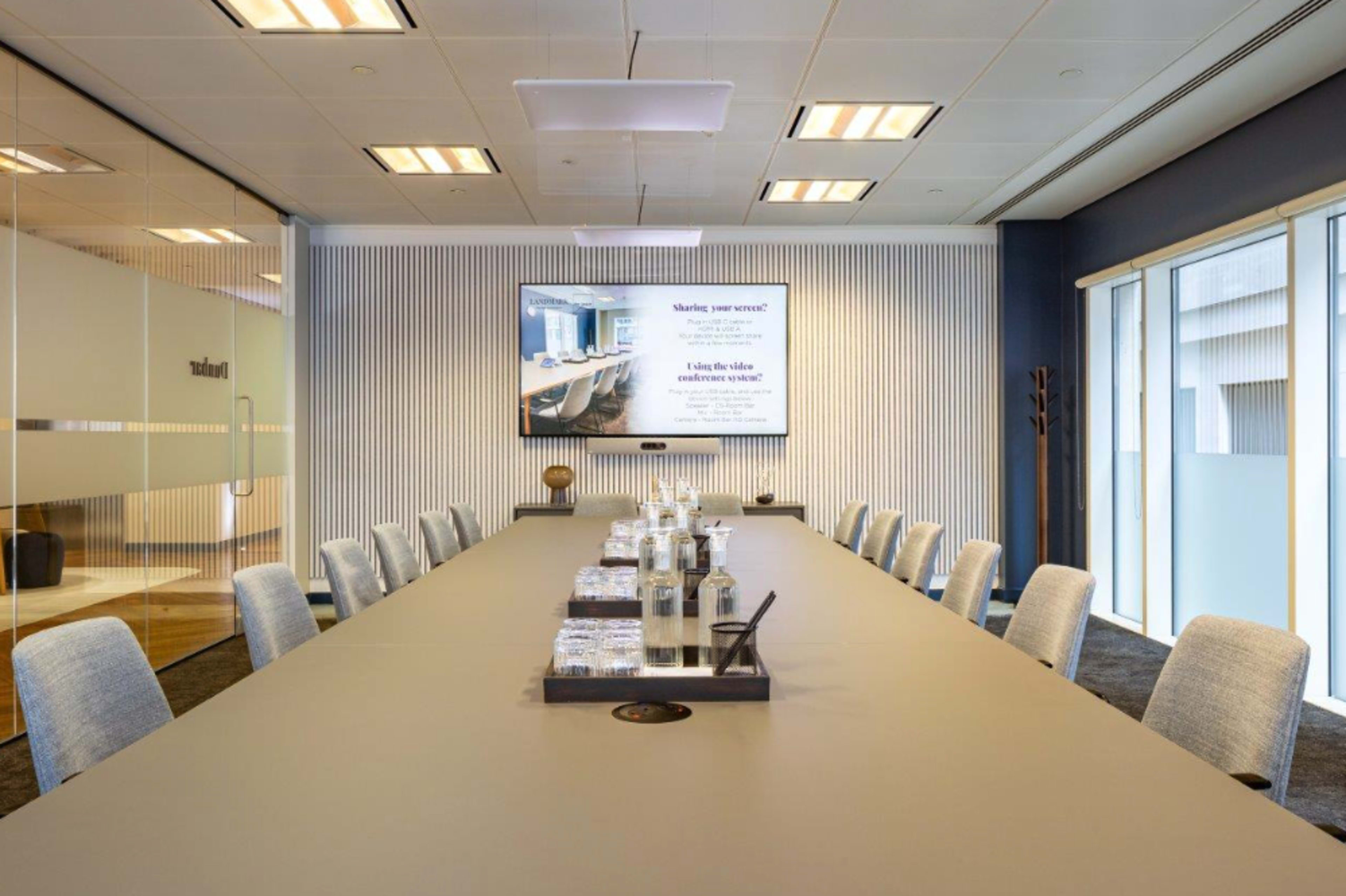 A modern conference room features a long table set with water bottles and glasses, along with a large screen displaying a presentation.