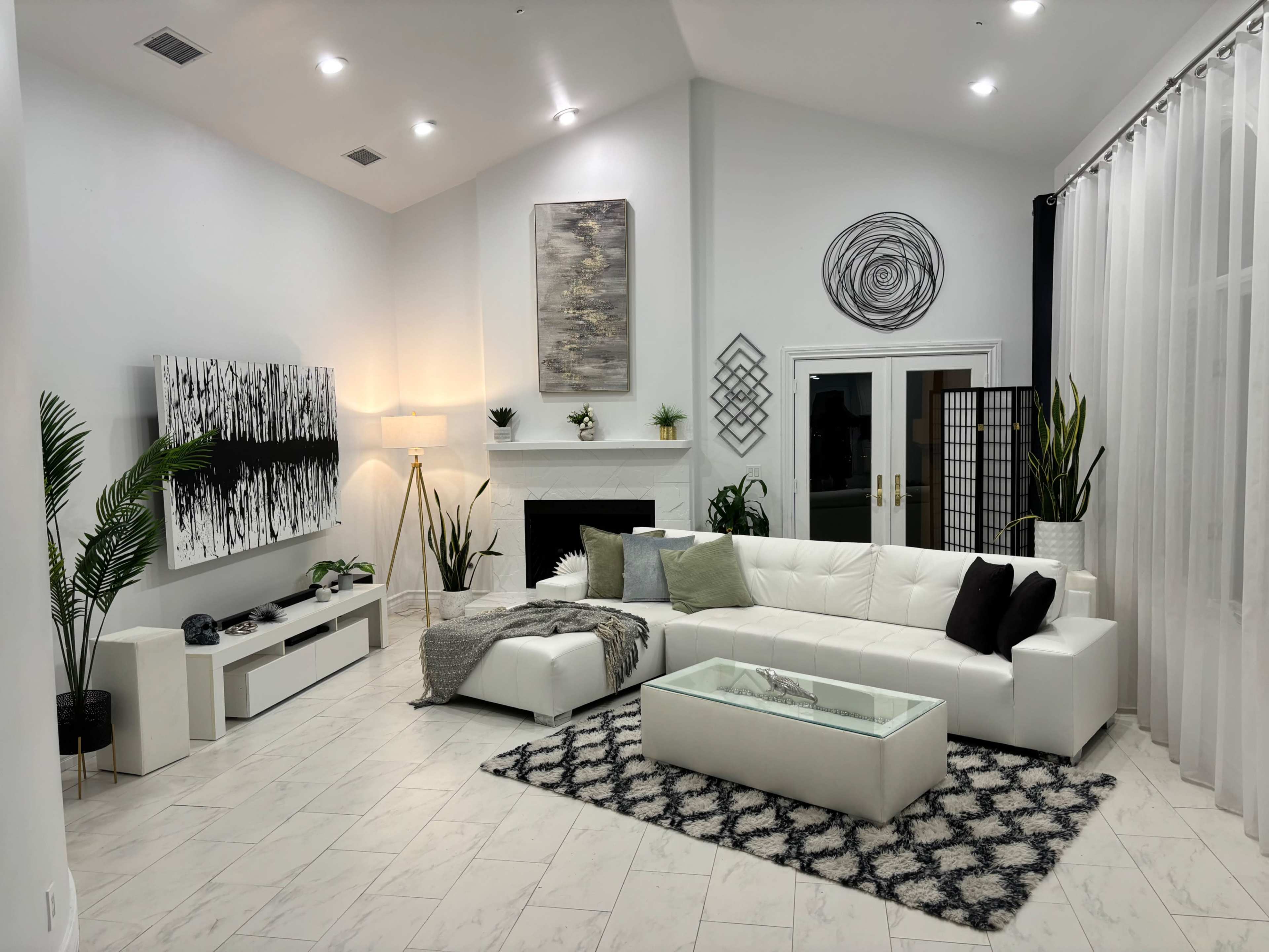 The image shows a modern living room featuring a large sectional sofa, a coffee table, and decorative elements like plants and artwork on the walls.