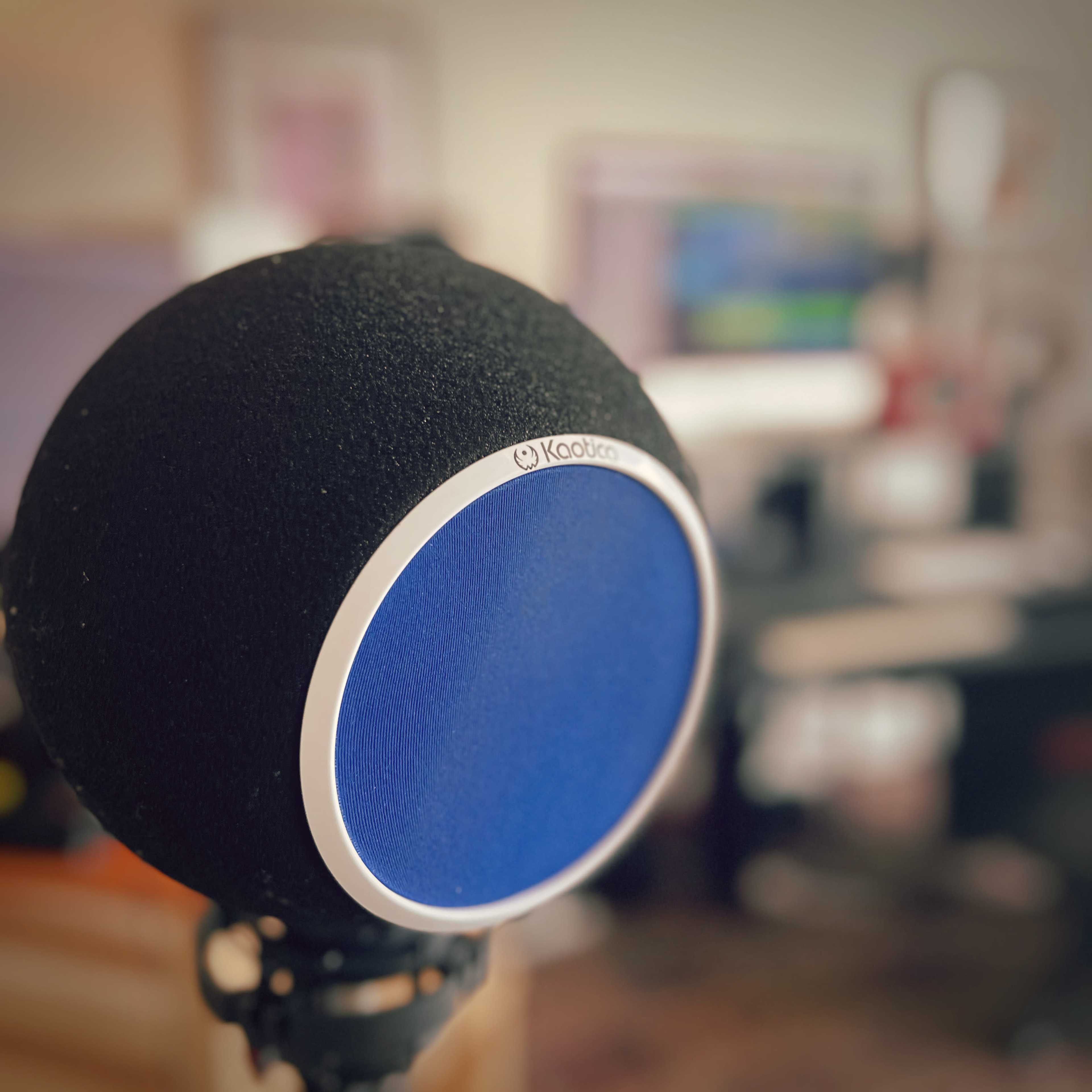 A microphone with a blue pop filter is prominently featured in a blurred home studio environment.