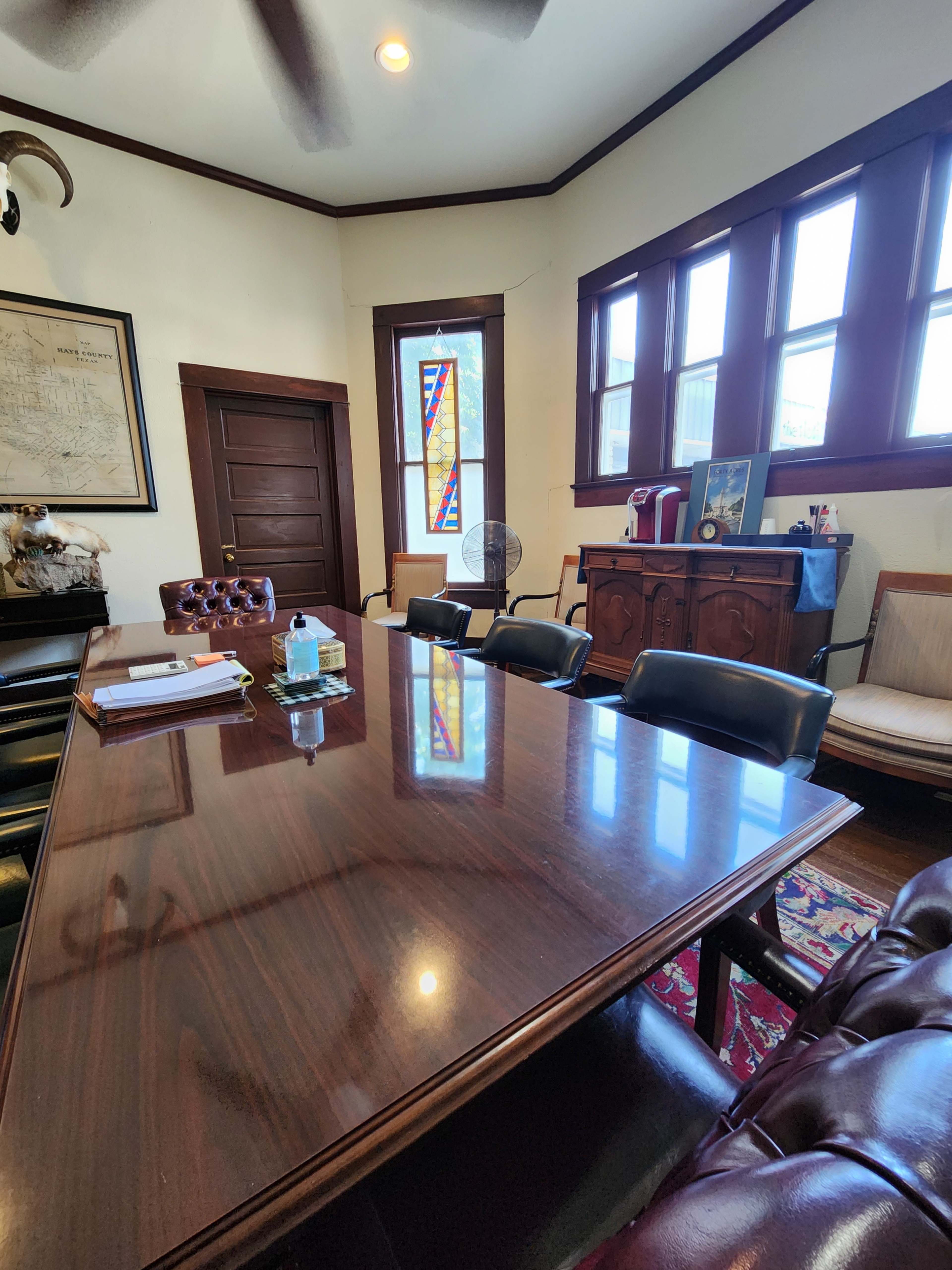 A conference room with a long wooden table, several black chairs, and a stained glass window in the background.