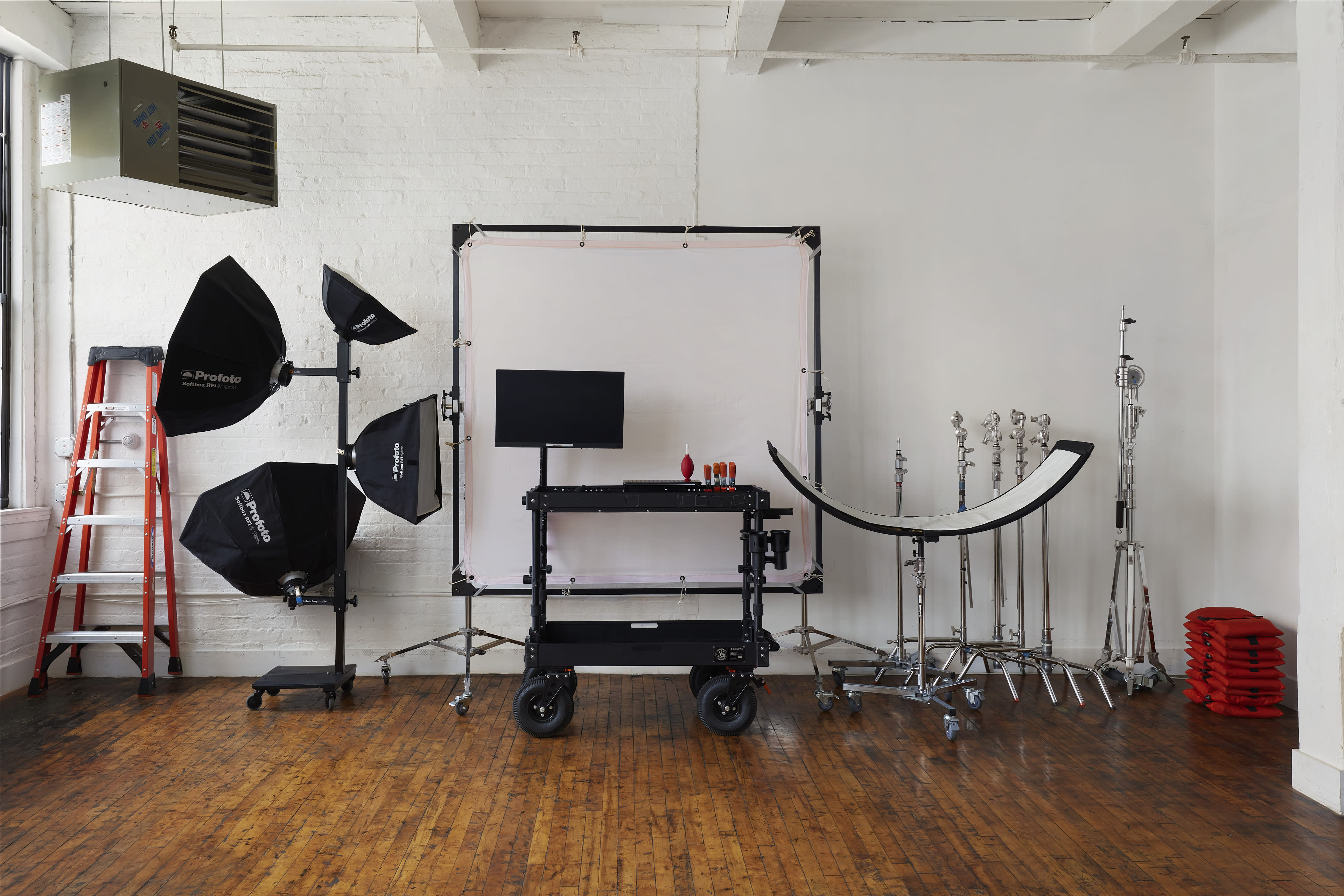 A photography studio setup featuring softbox lights, a backdrop, a monitor on a cart, and various light stands on a wooden floor.