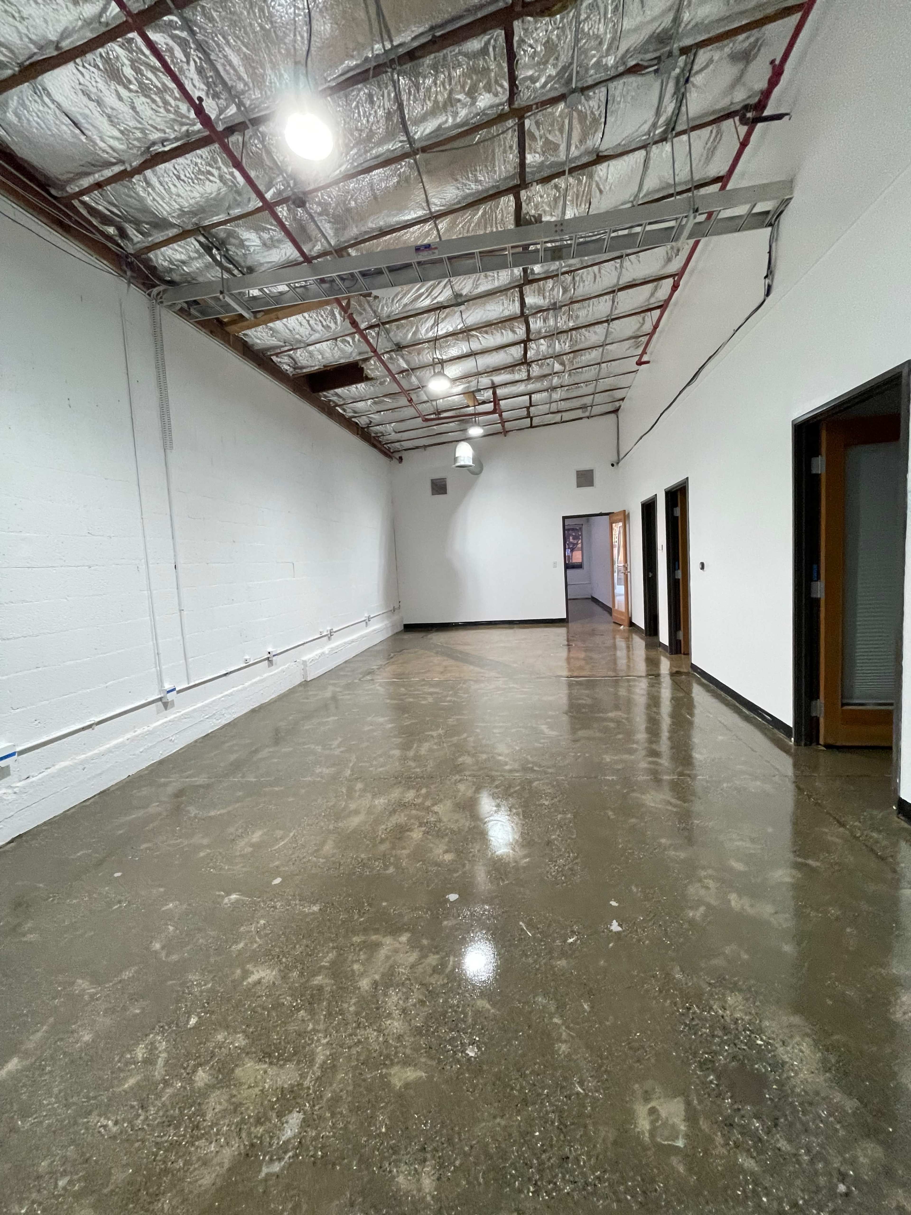 The image shows a long, empty hallway in a commercial building with polished concrete floors and white walls.
