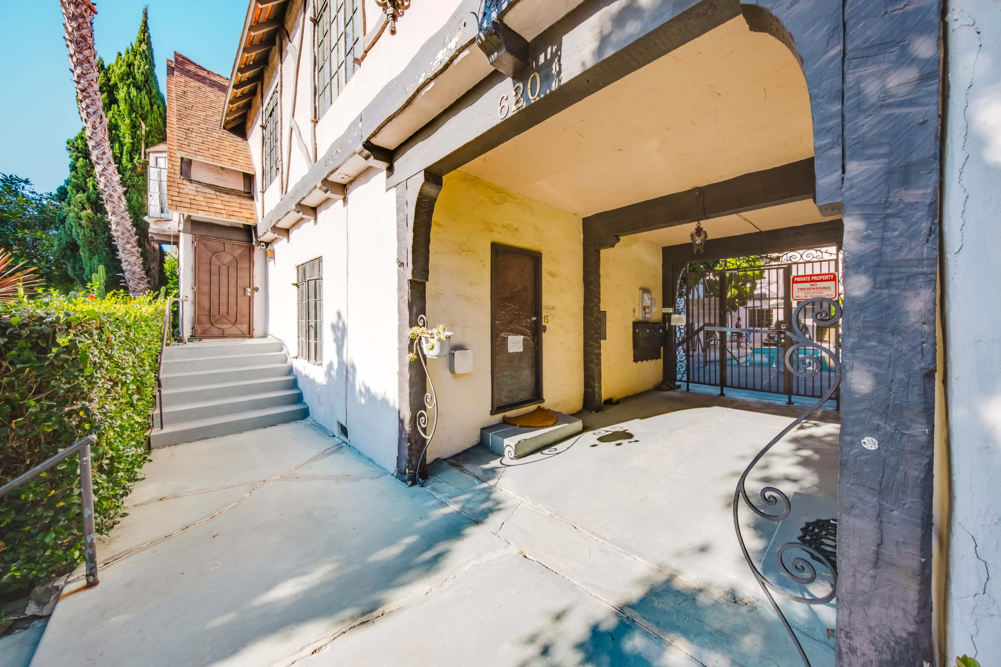 The image shows a residential property with an arched entrance leading to a gated parking area and a staircase on the left.