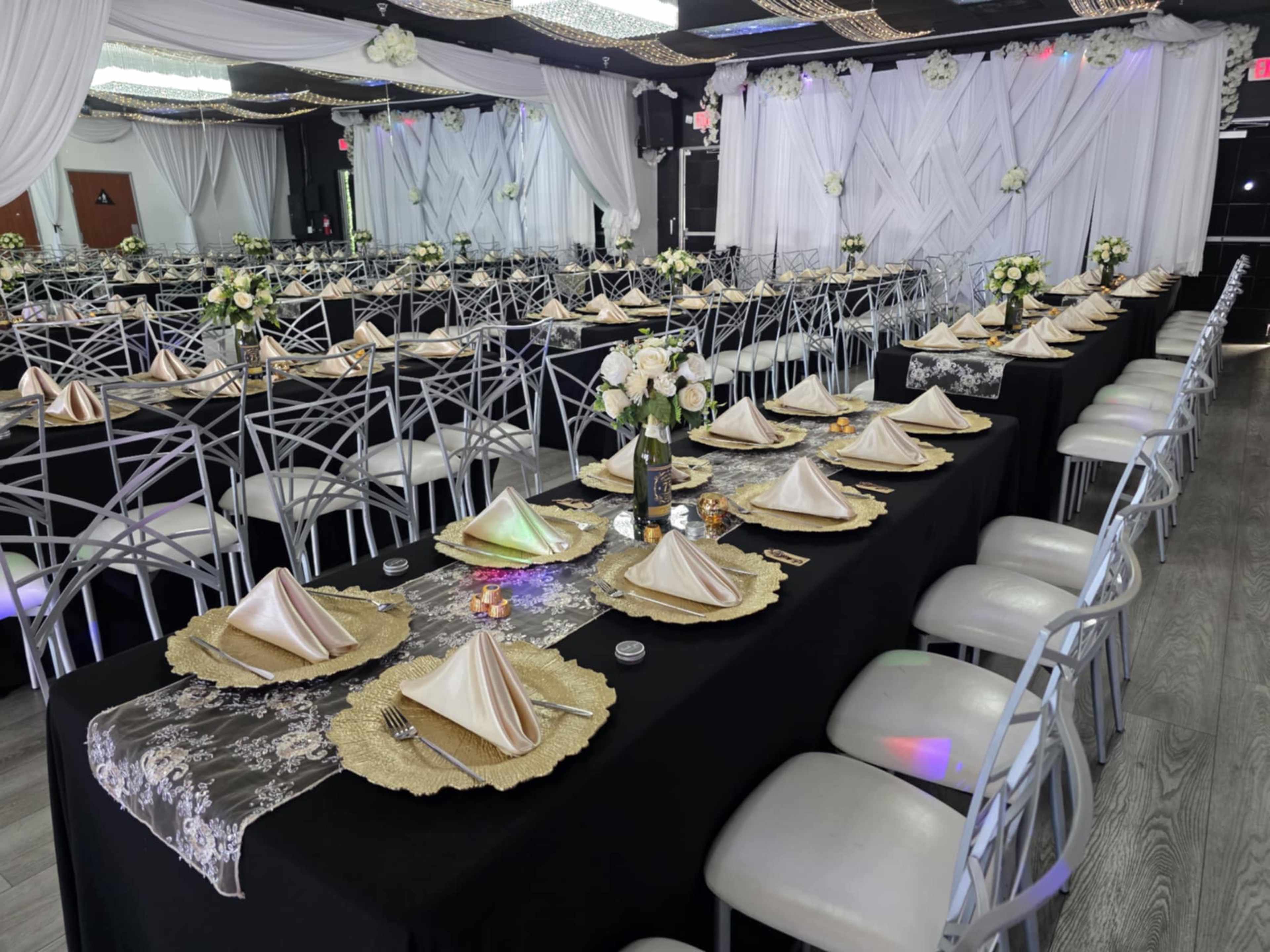A banquet hall featuring multiple rows of elegantly set tables with gold and black decorations, complete with folded napkins and floral centerpieces.
