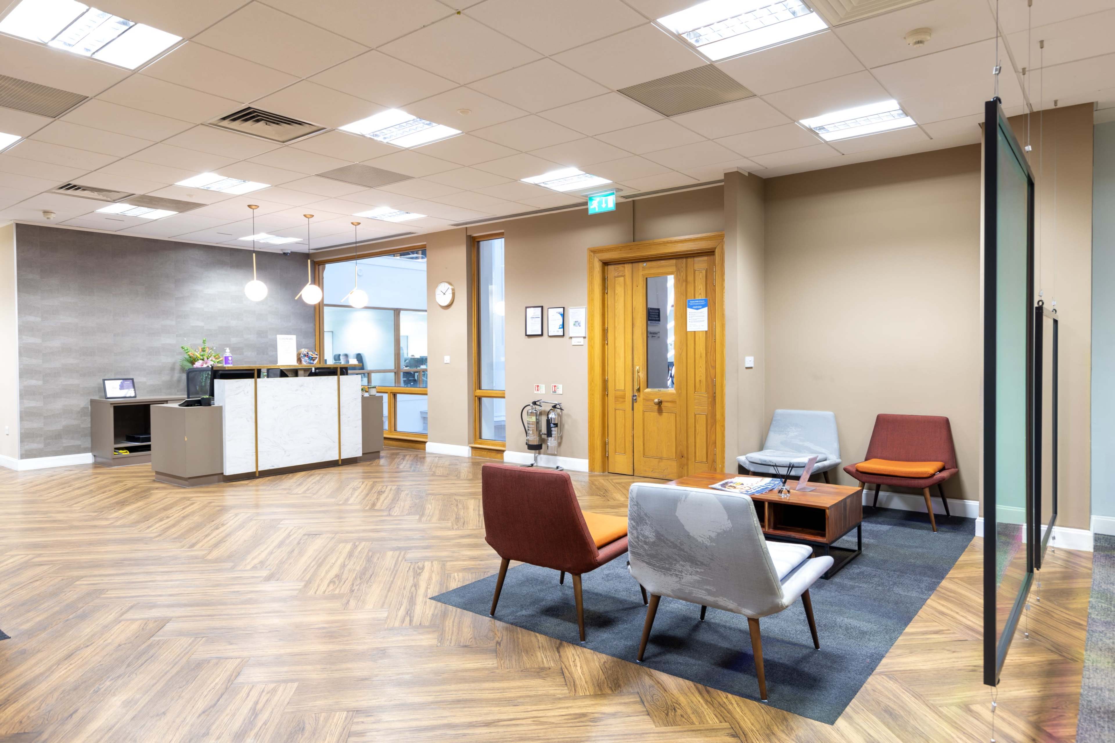 A modern office reception area with a seating arrangement, a reception desk, and wooden flooring.