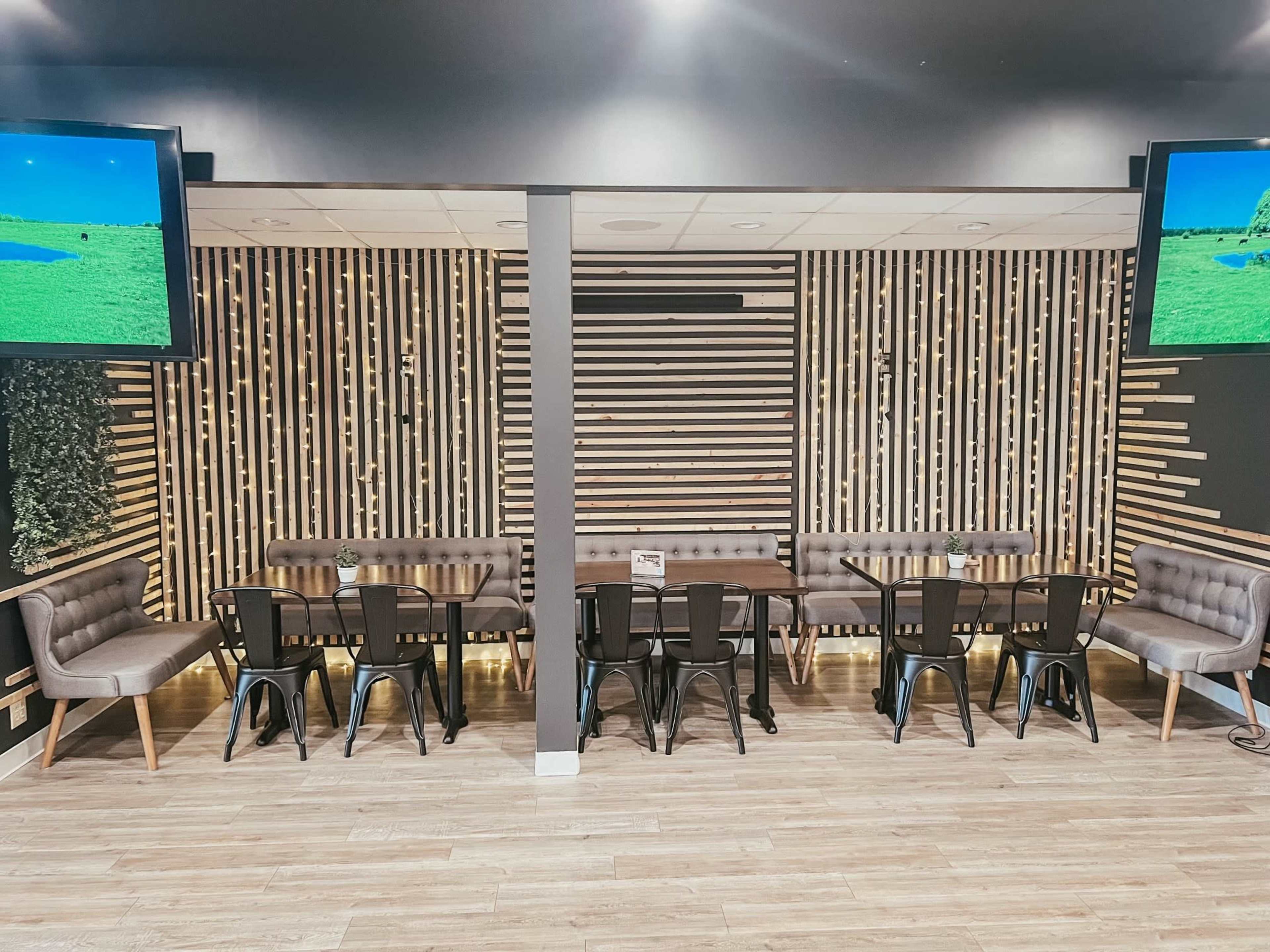A modern dining area featuring tables and chairs arranged against a backdrop of wooden slats and large screens displaying scenic images.