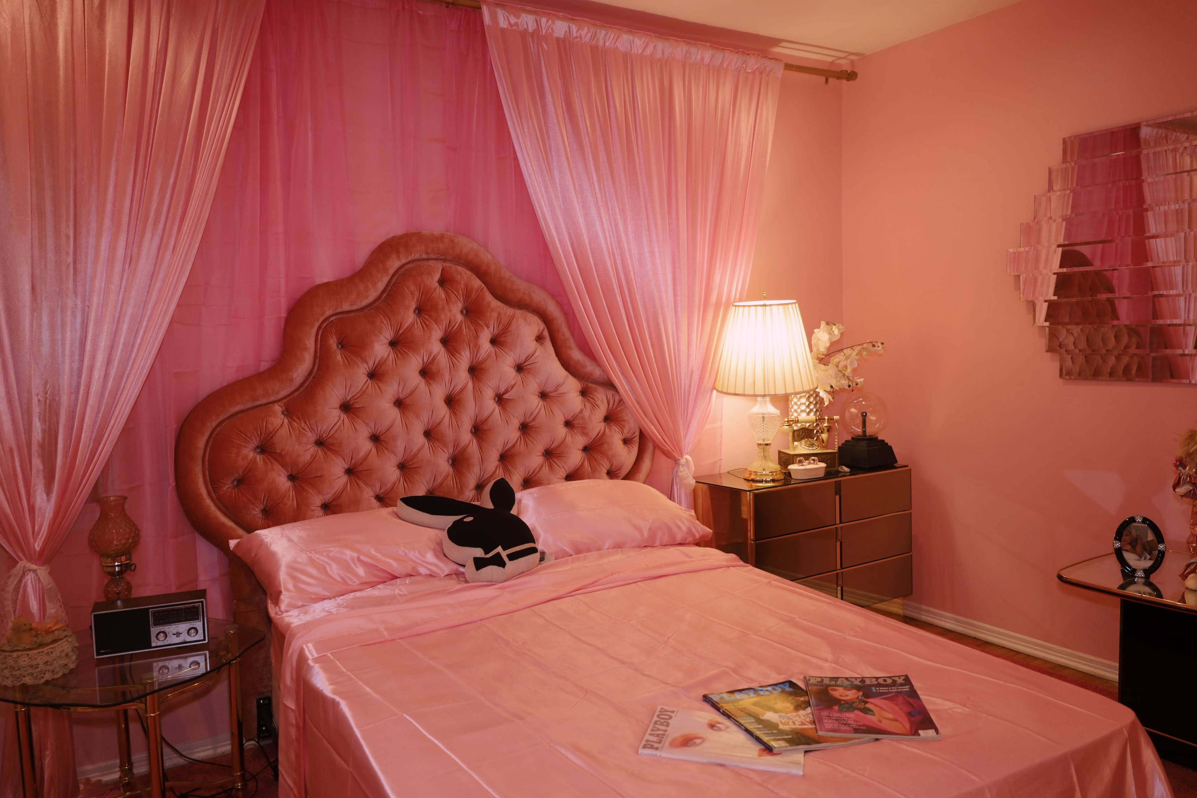 The image showcases a pink-themed bedroom featuring a tufted bed with a bunny-shaped pillow, sheer curtains, and a mirrored nightstand.
