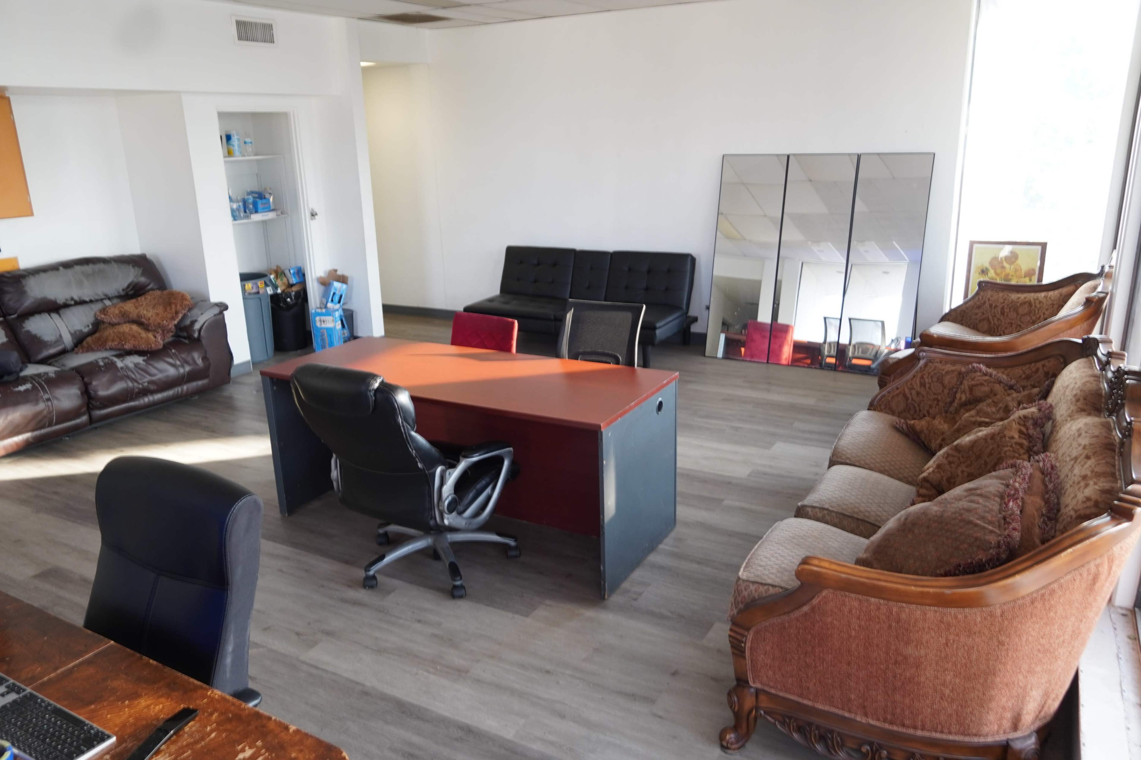 The room features a central desk with a swivel chair, surrounded by various seating options including sofas and a large mirror against the wall.