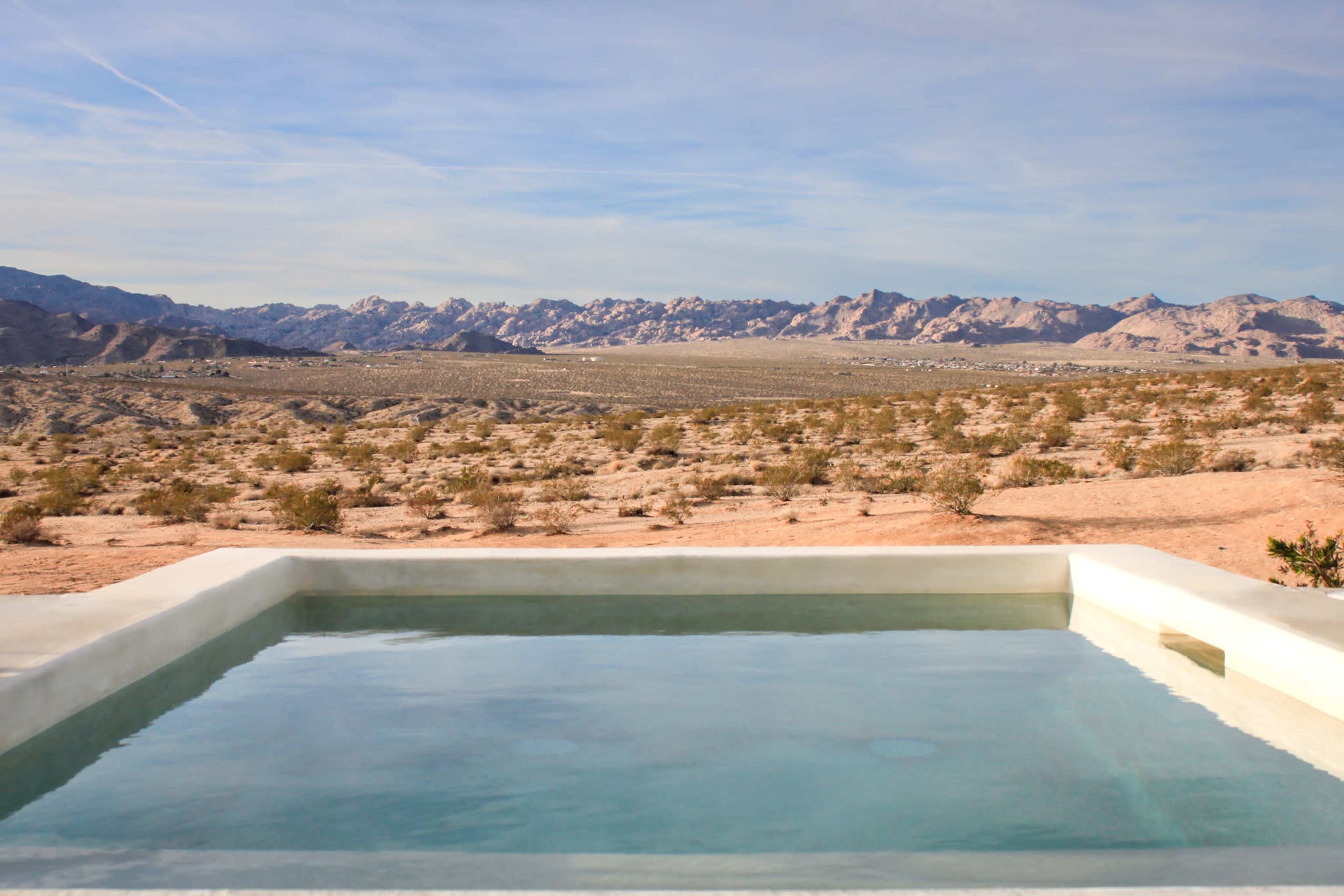 A rectangular pool sits on a desert plateau with distant mountains and sparse vegetation in the background.