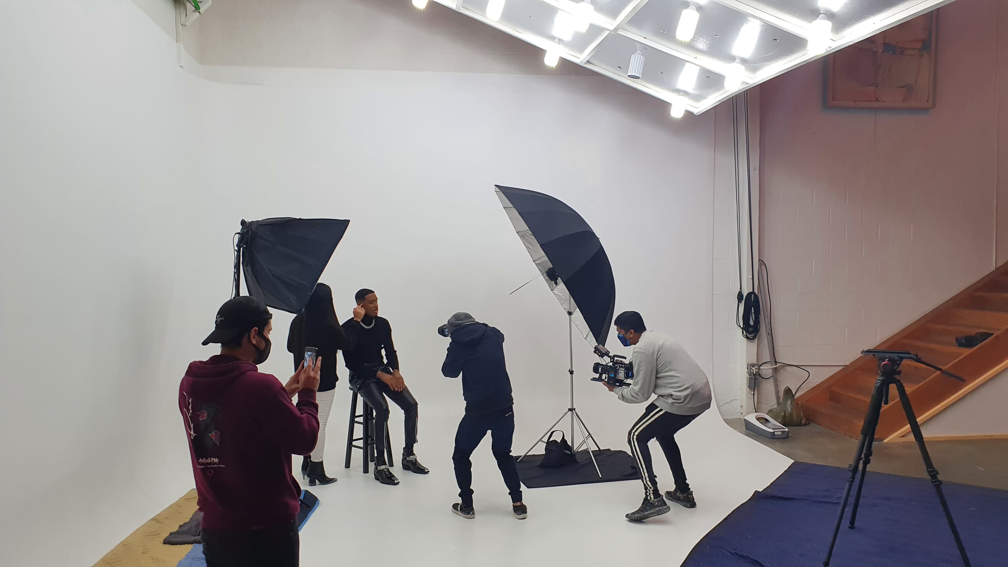 A group of people is filming a photoshoot in a studio with large softbox lights and a plain white background.