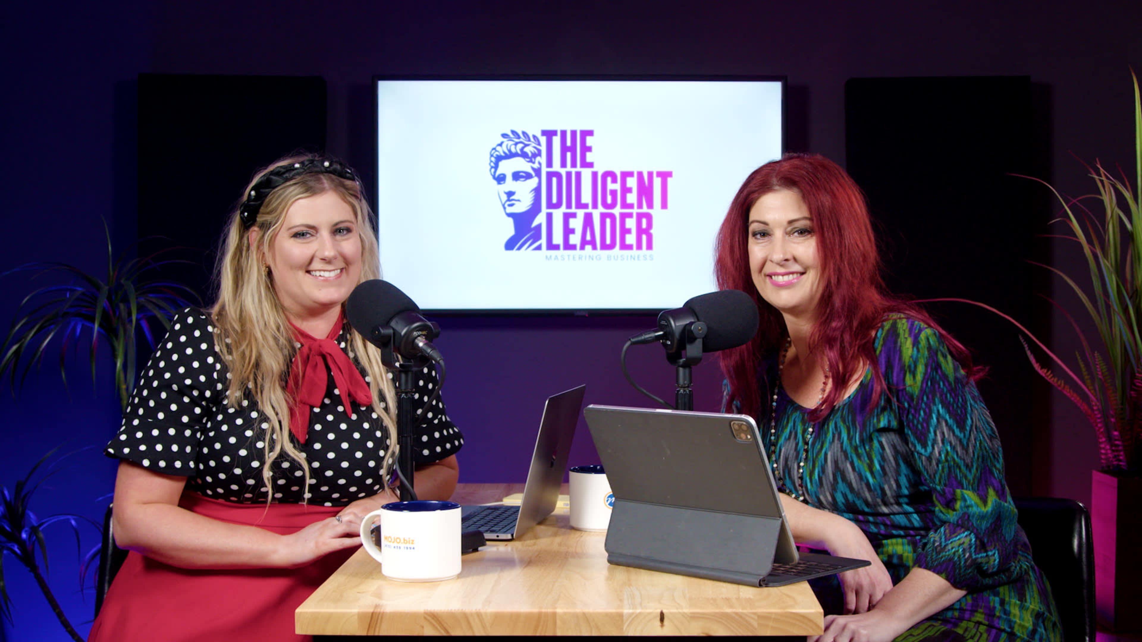 Two women sit at a table with microphones in front of them, smiling while discussing topics related to business, with a logo for "The Diligent Leader" displayed on a screen behind them.