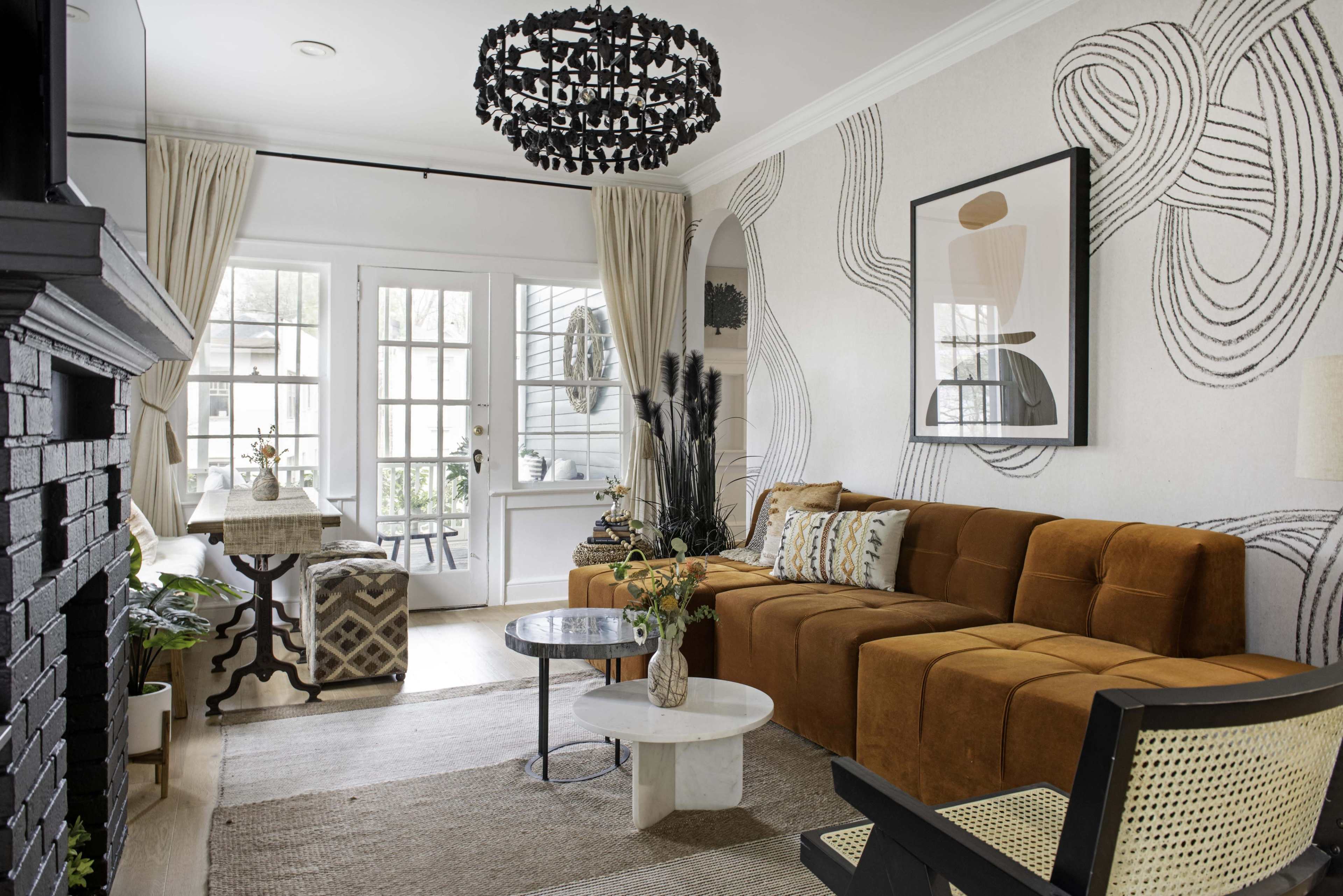 The image shows a modern living room with a brown sectional sofa, a round coffee table, and large windows illuminated by natural light.