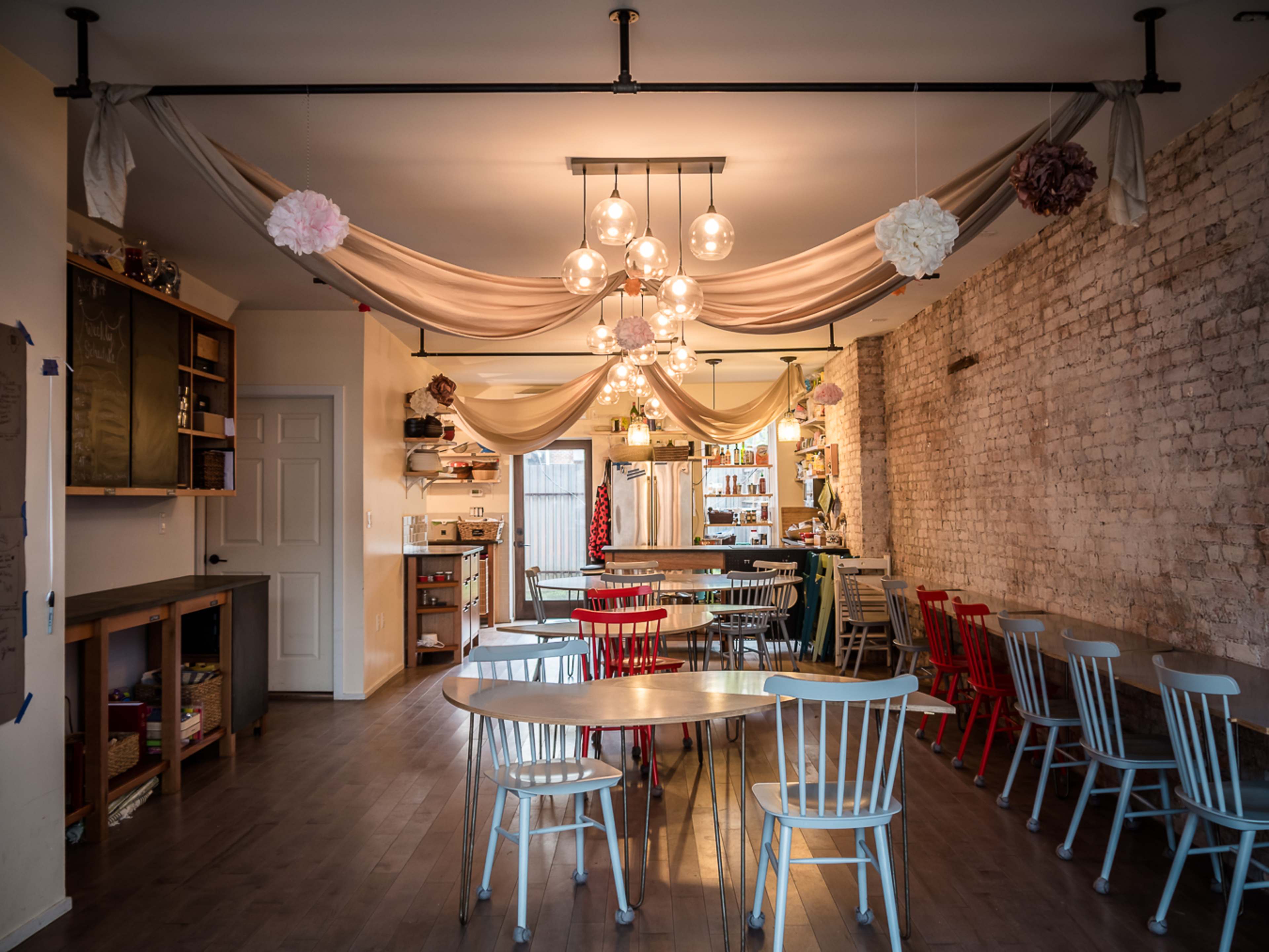 A cozy café interior with wooden tables, colorful chairs, and decorative lighting hanging from the ceiling.