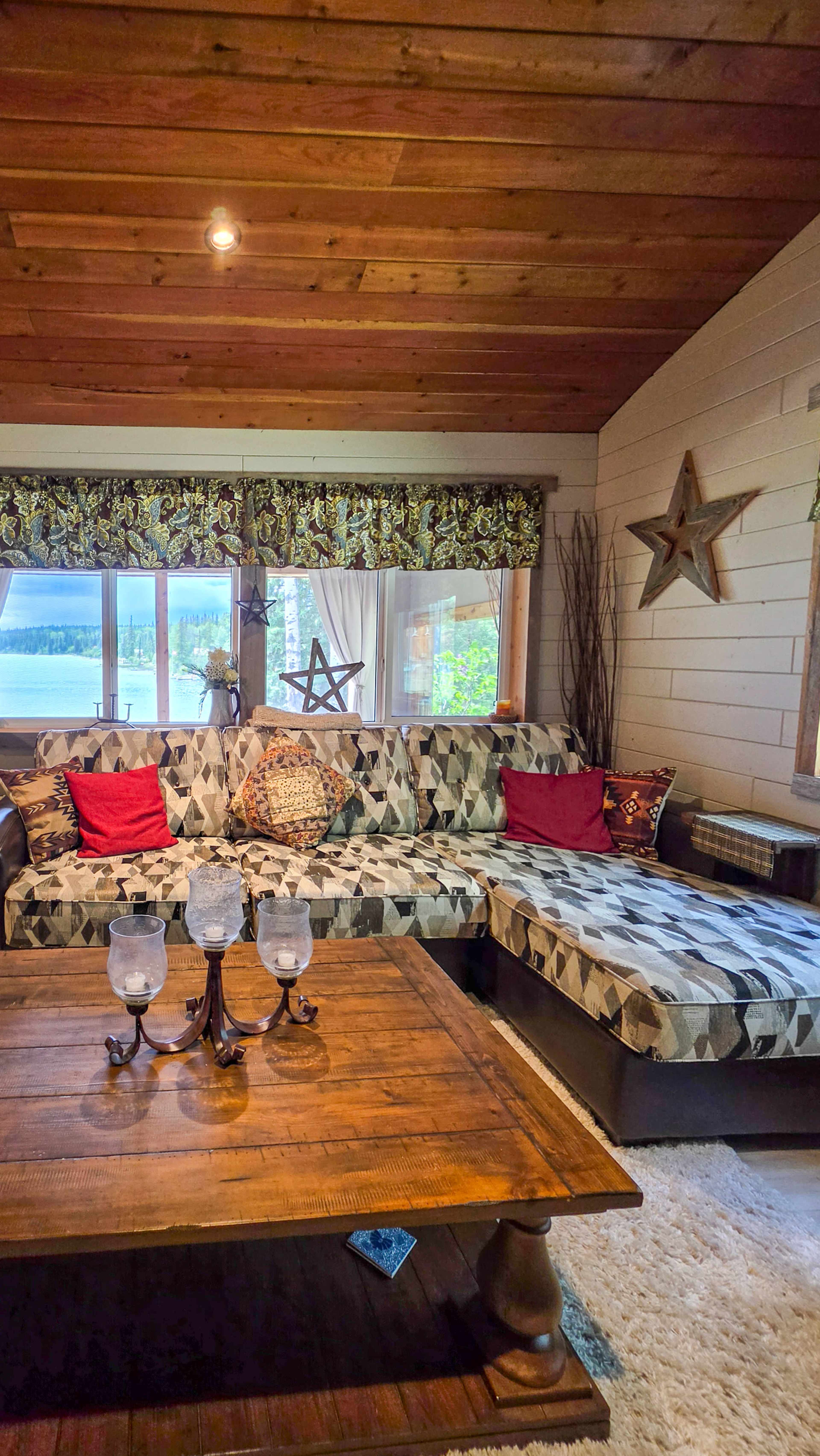 The image shows a cozy living room with a sectional sofa, a wooden coffee table, and large windows overlooking a body of water.