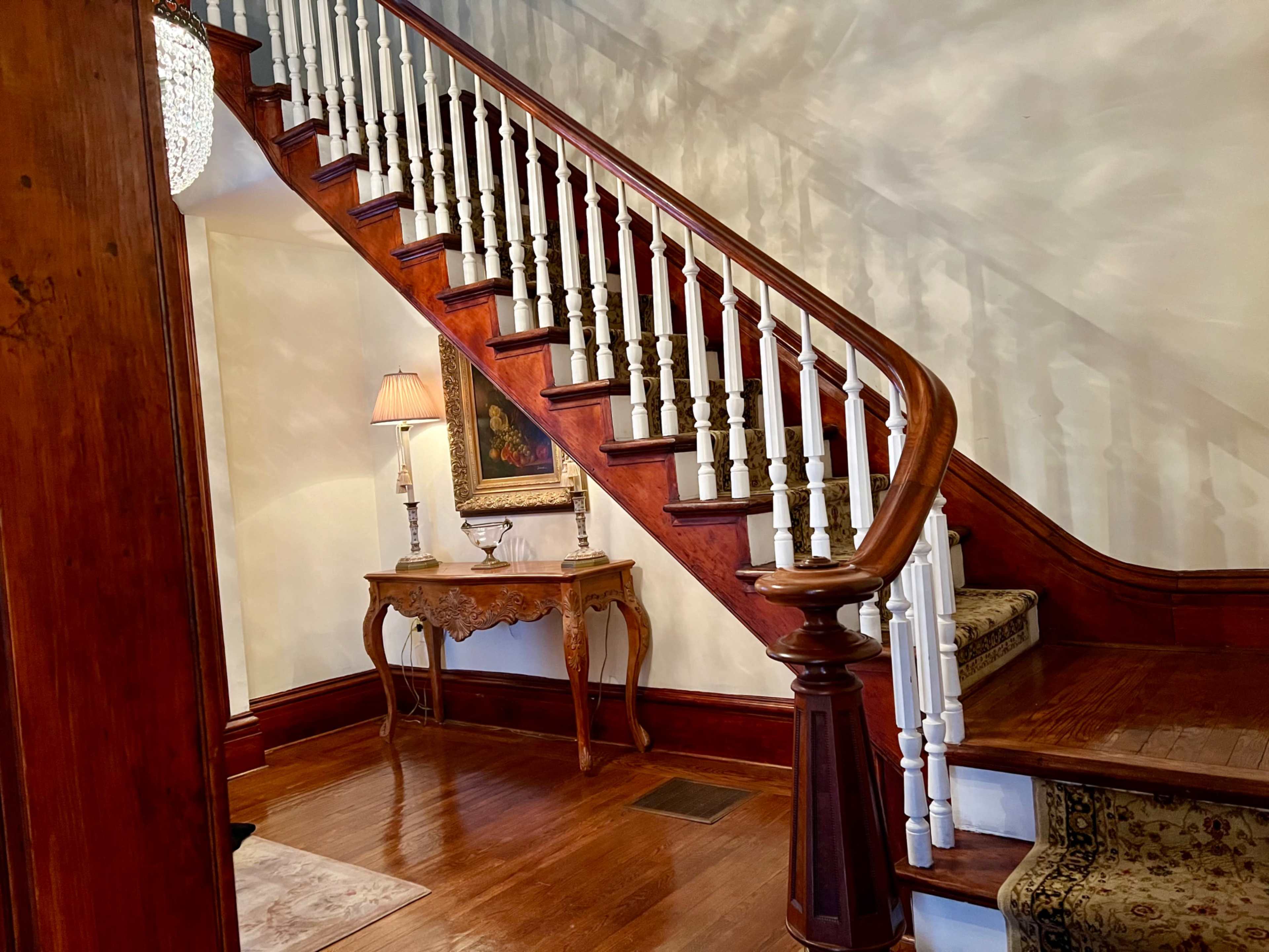 A wooden staircase with white balusters leading to an upper level, adjacent to a foyer with an elegant table and a lamp.