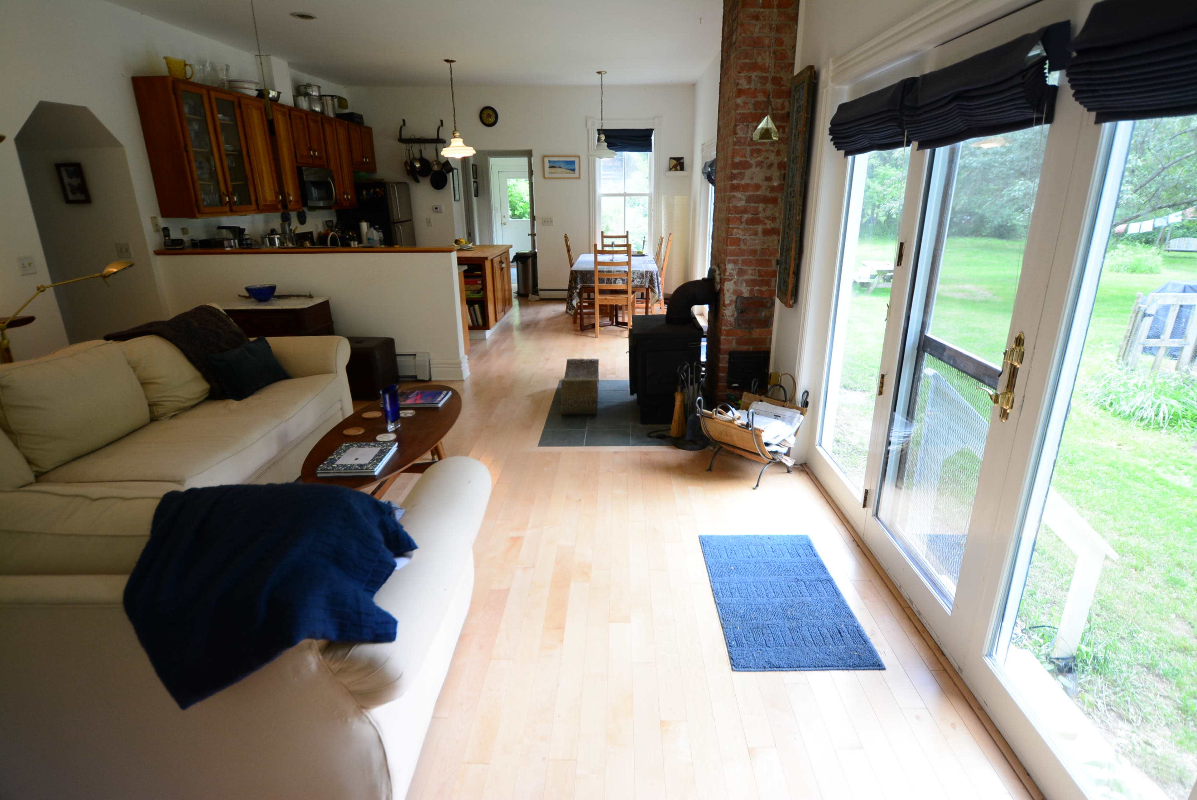 The image shows a spacious living room with wooden floors, a white couch, and large glass doors leading to a garden area.