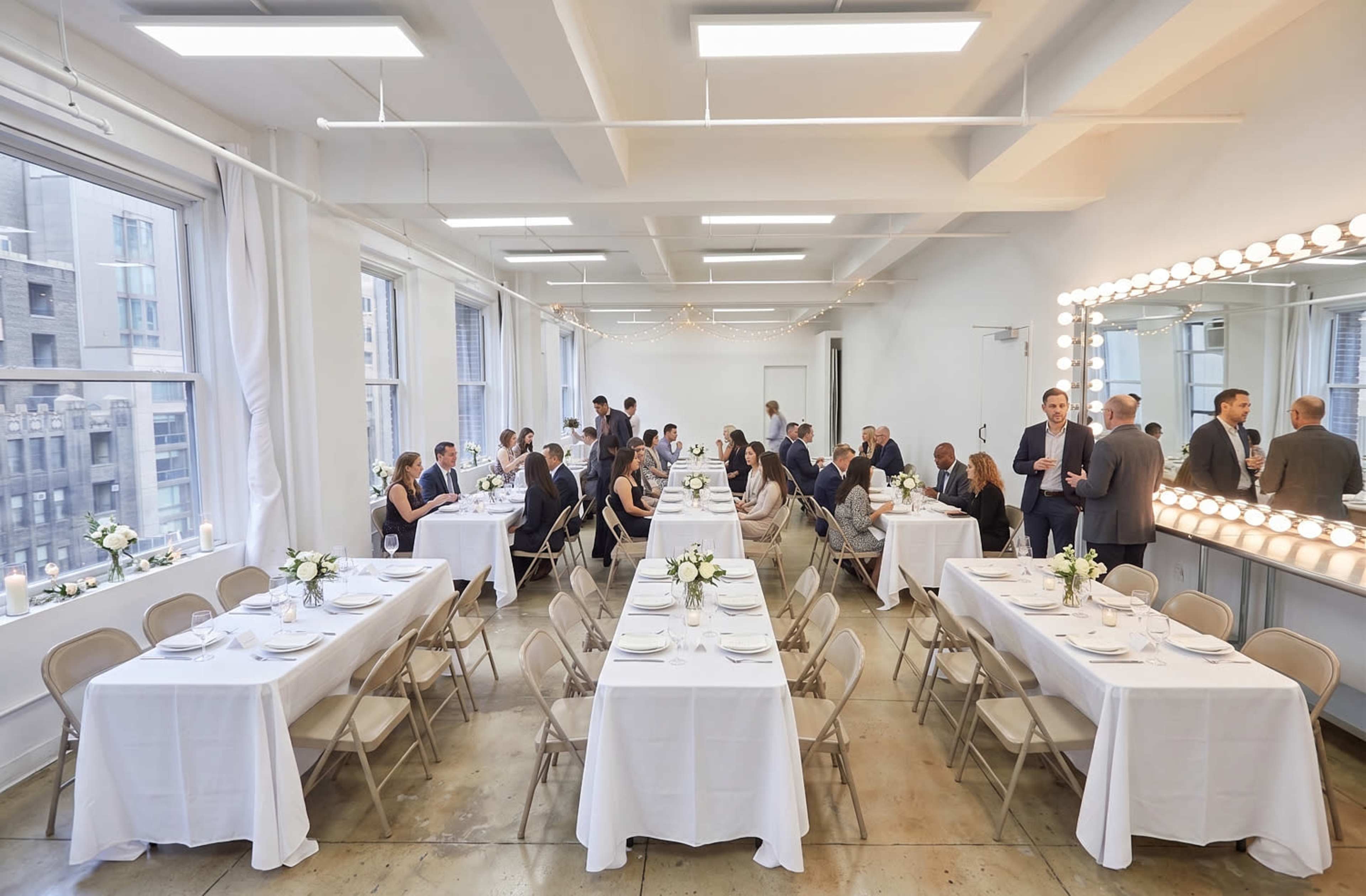 A spacious dining area features elegantly set tables with white linens and centerpieces, accommodating several groups of guests engaged in conversation.