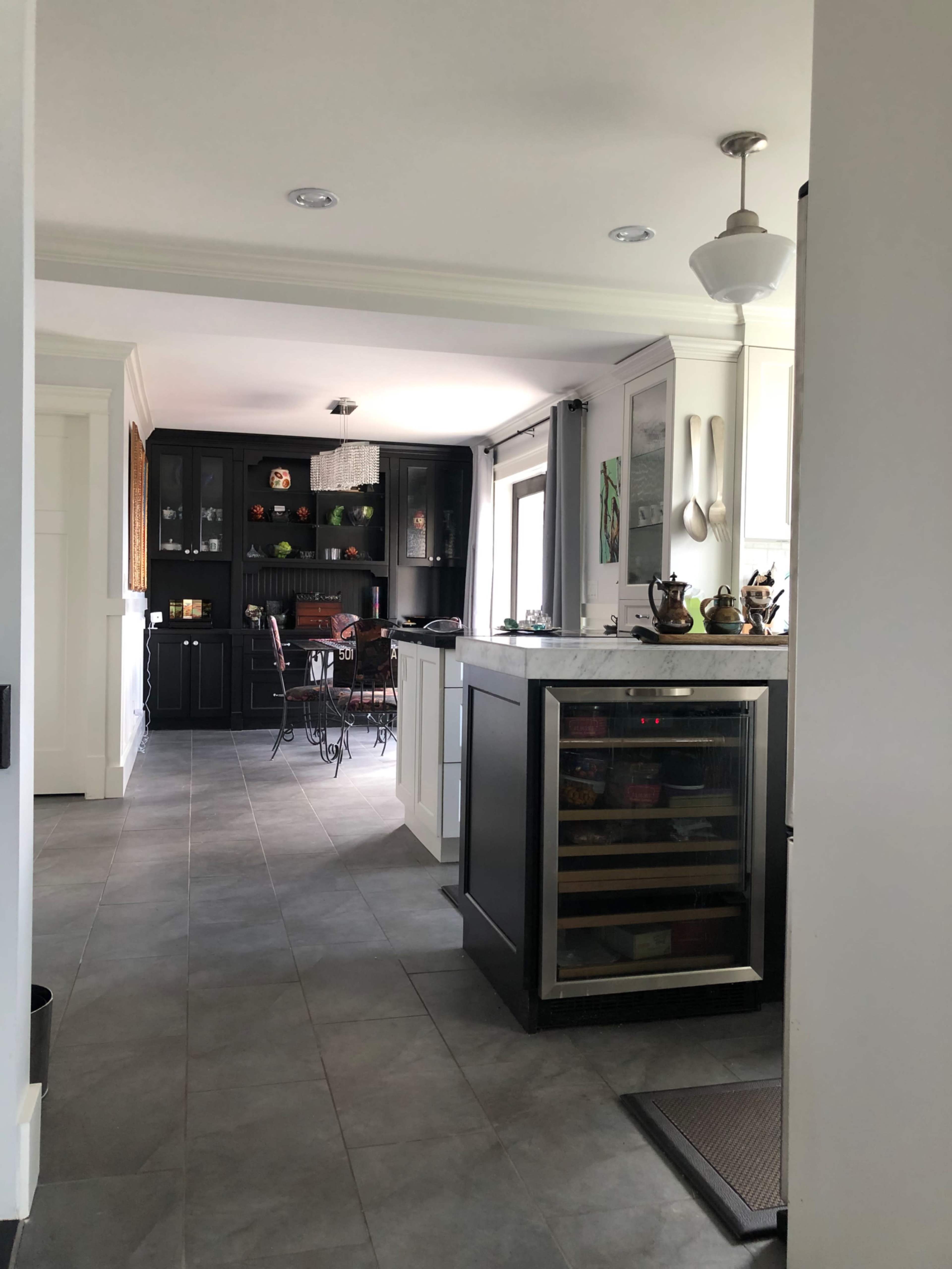 A modern kitchen with dark cabinetry, a countertop wine cooler, and a dining area visible in the background.