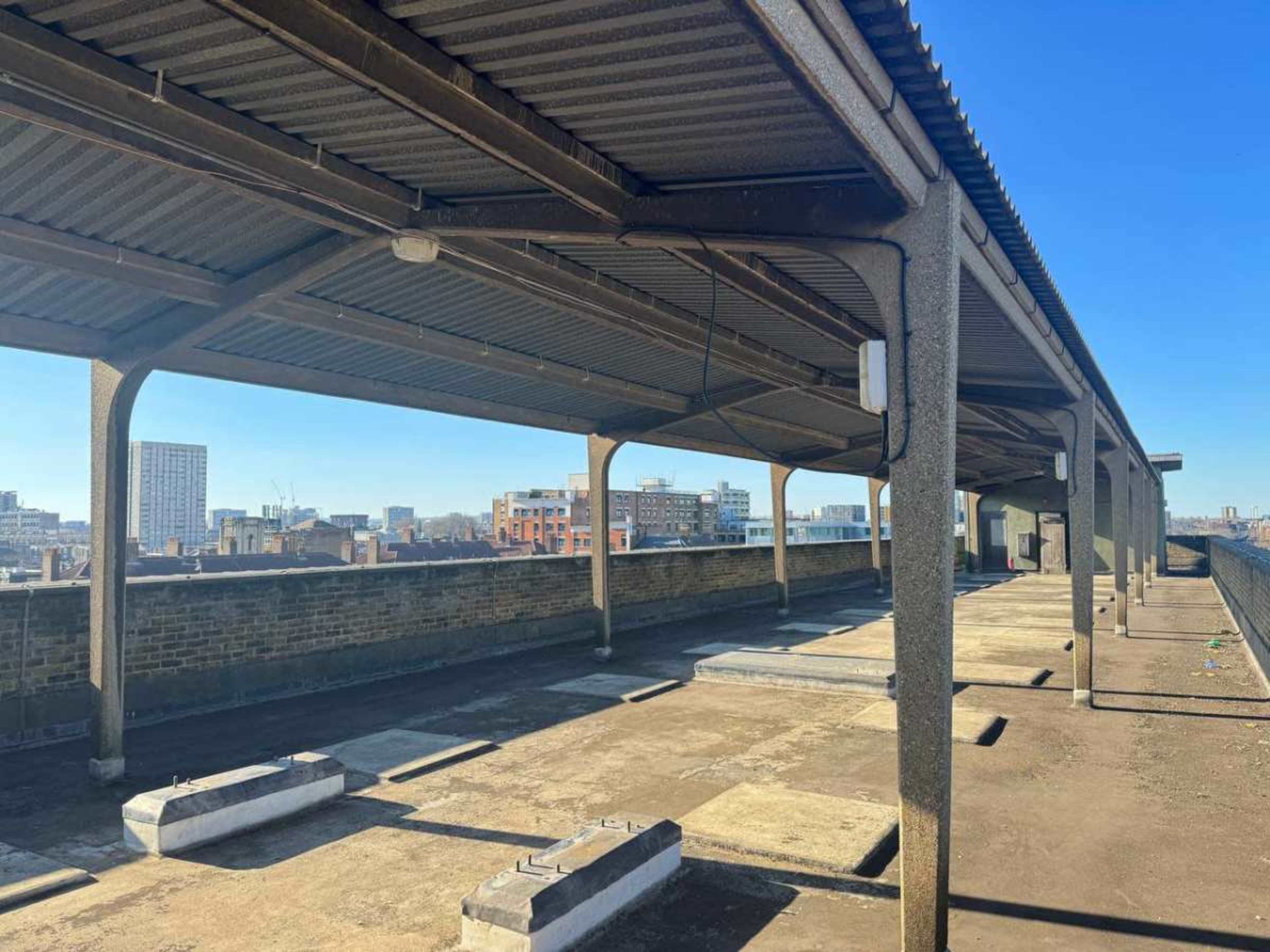 The image shows a rooftop area with a metal covering, concrete surfaces, and a view of city buildings in the background.