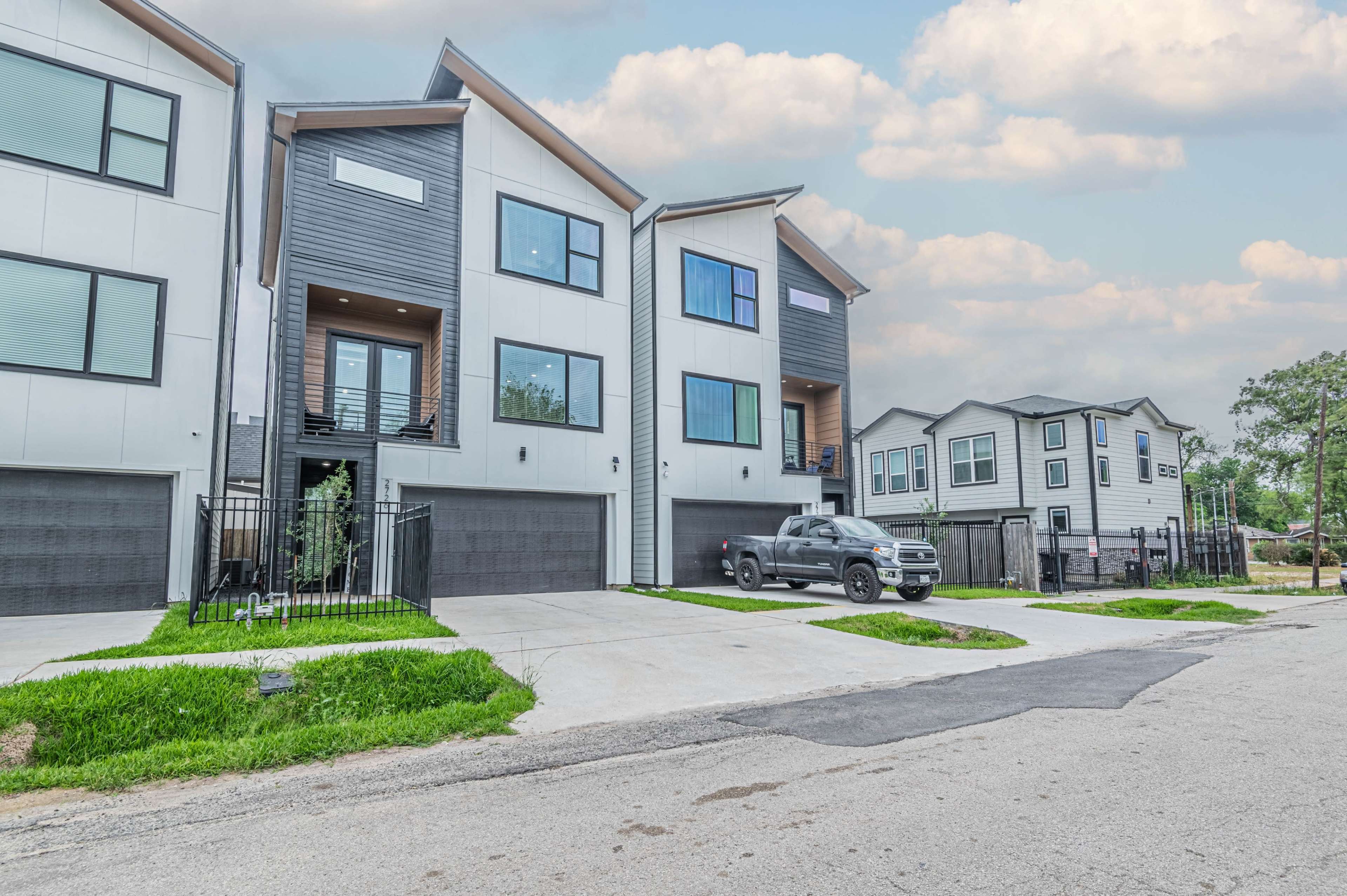 A row of modern two-story houses with a gray pickup truck parked in front of one on a paved street.