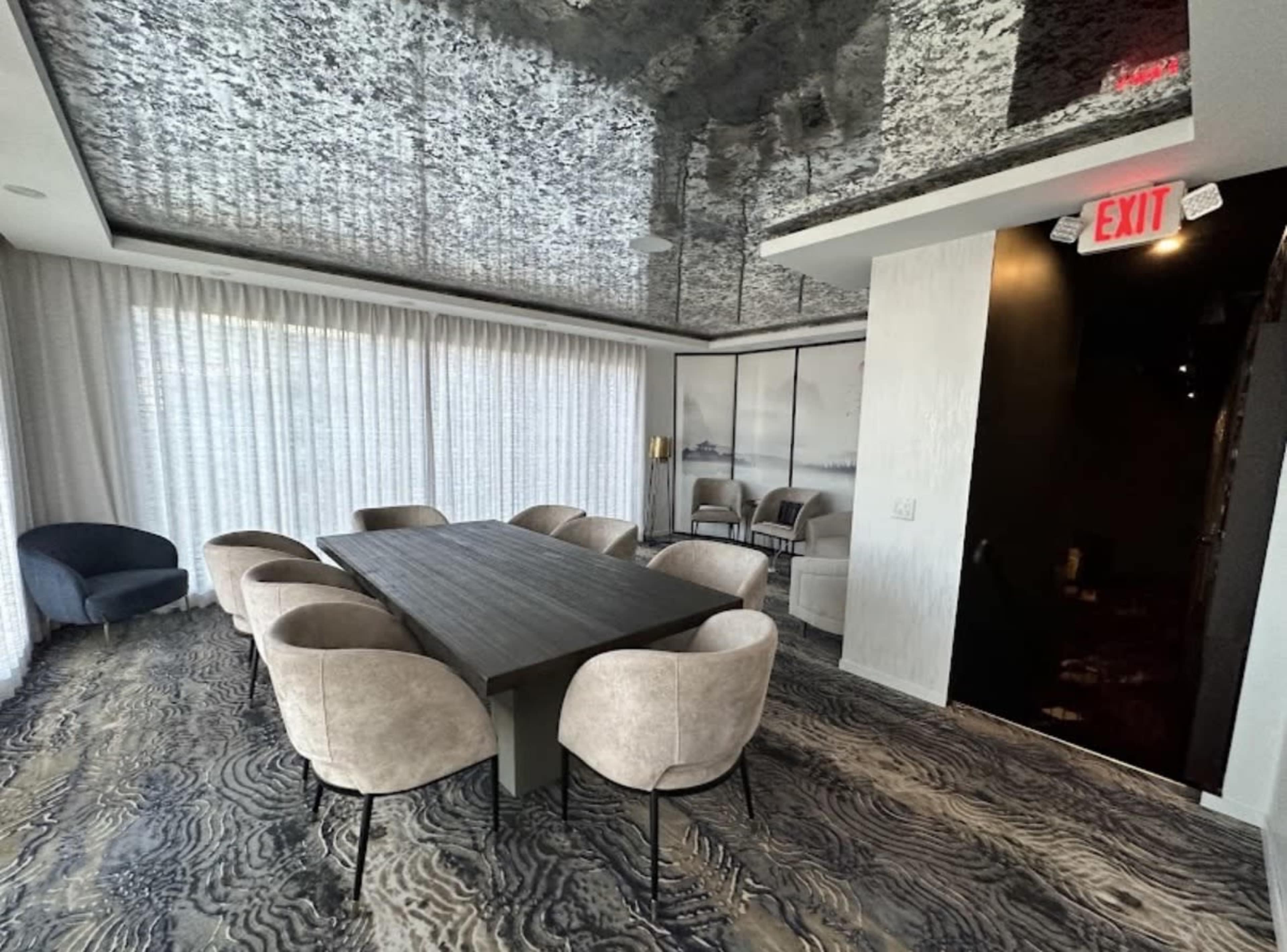 A modern conference room features a large table surrounded by upholstered chairs, with floor-to-ceiling curtains and a ceiling that reflects the room's design.
