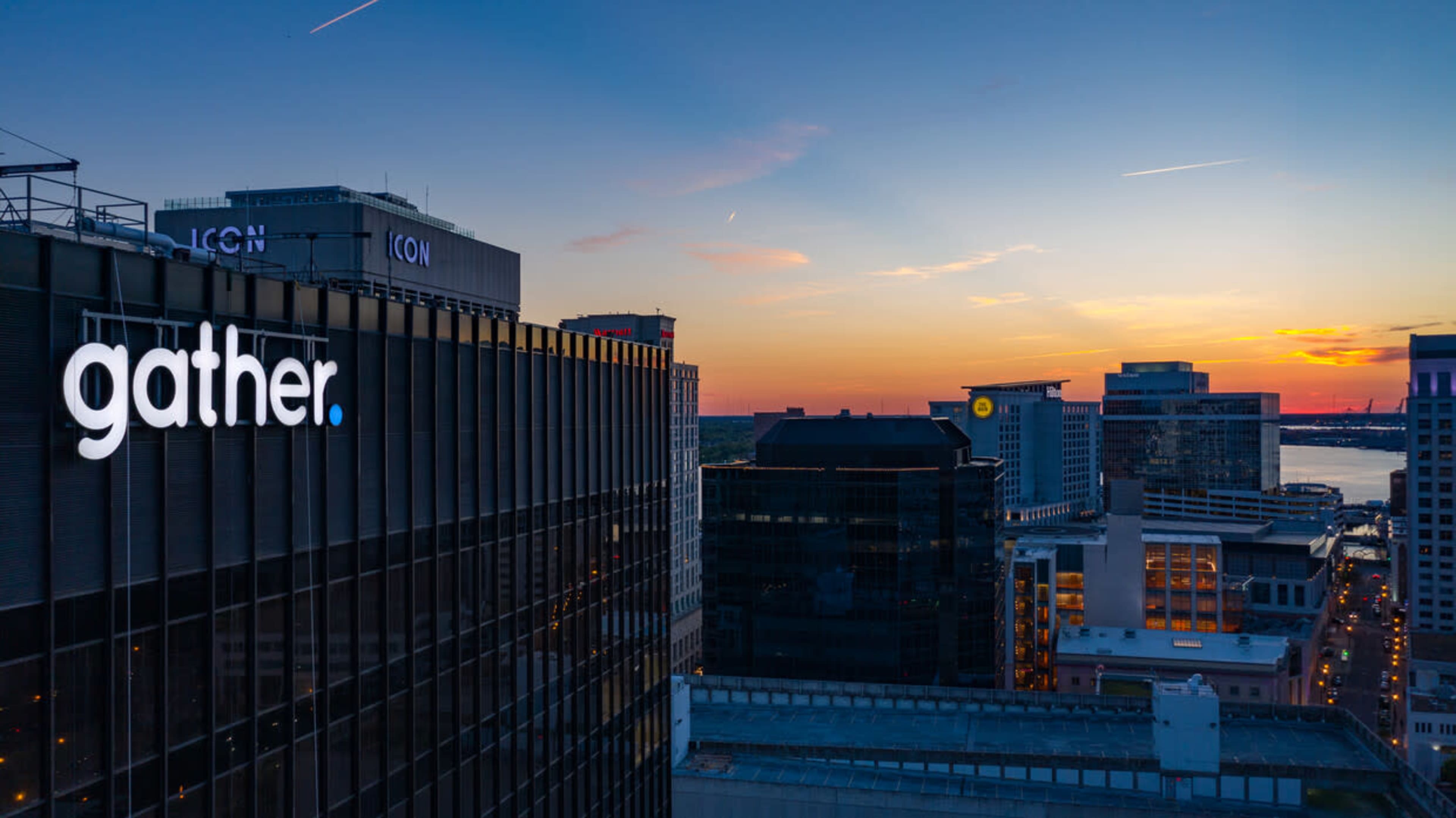 The image shows a high-rise building with the word "gather" illuminated on its facade, set against a colorful sunset skyline.