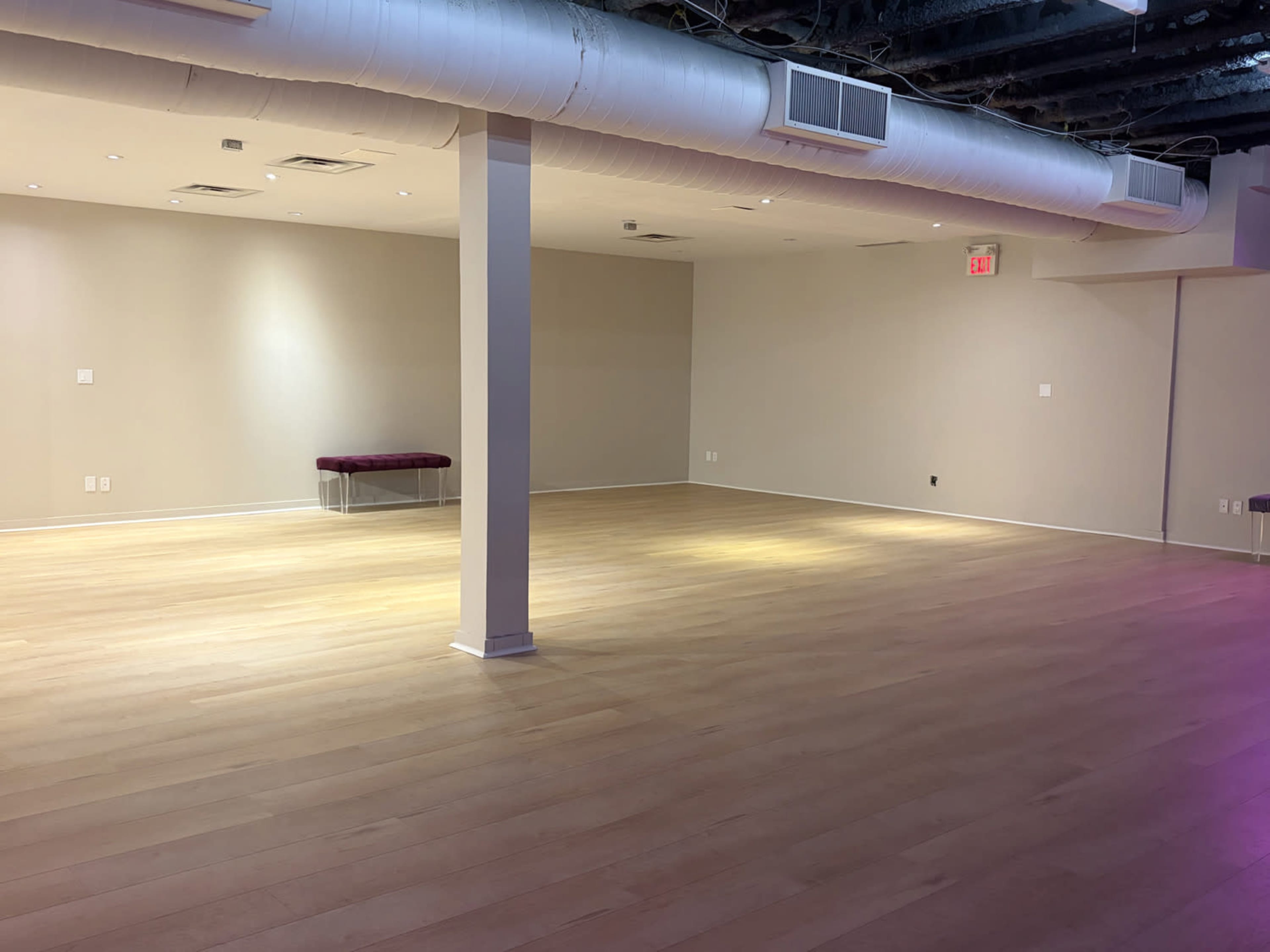 The image shows a spacious, empty room with wooden flooring, a single column, and soft lighting.