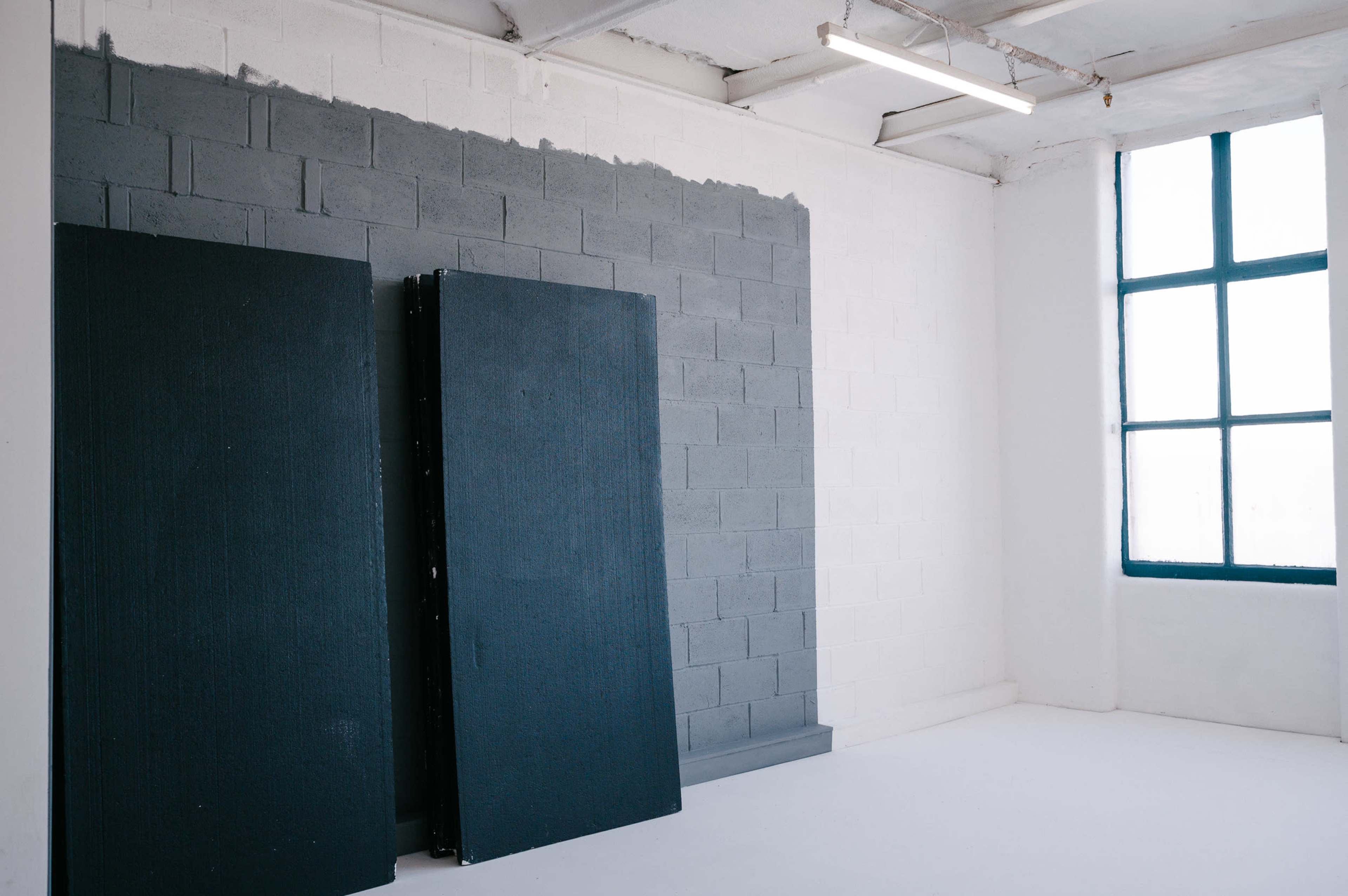 Two large black panels leaning against a gray and white painted wall with a window featuring blue trim.